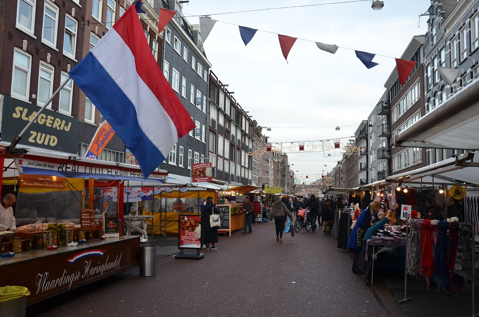 The Albert Cuypmarkt street lined with stalls, including a herring stand, under strings of bunting and a Dutch flag