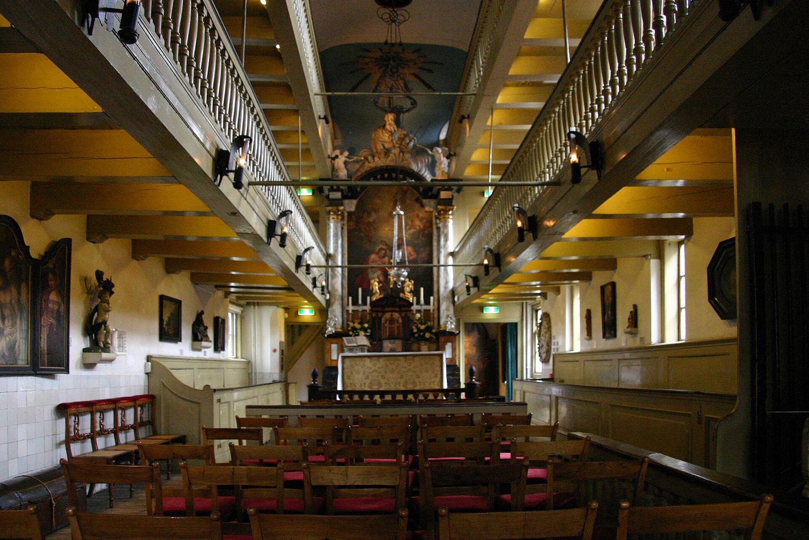 The attic church at Our Lord in the Attic: rows of wooden chairs facing a painted altar, with two tiers of wooden galleries along both sides under the roof beams
