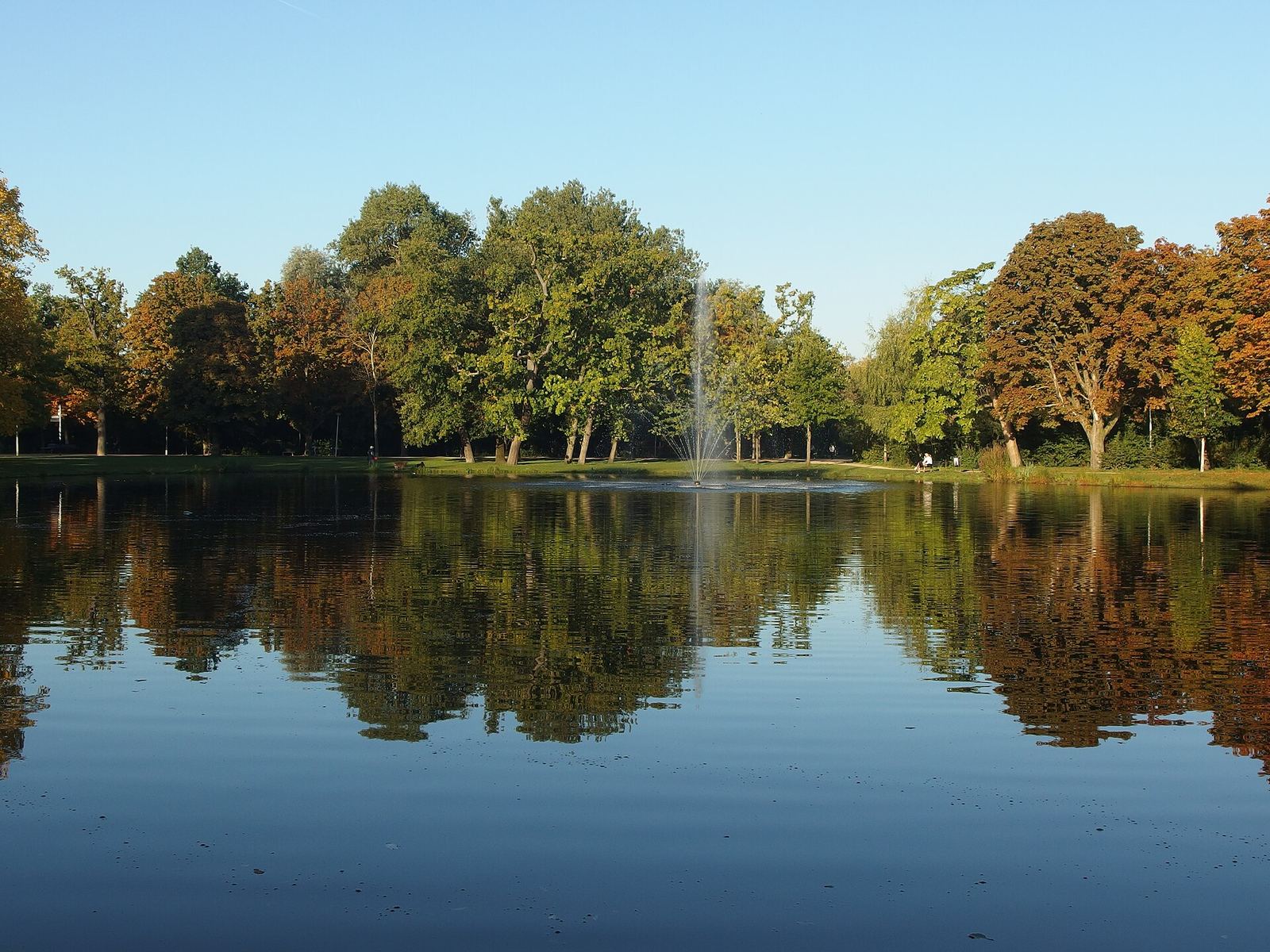 A pond in the Vondelpark reflecting trees turning orange and gold, with a fountain in the middle