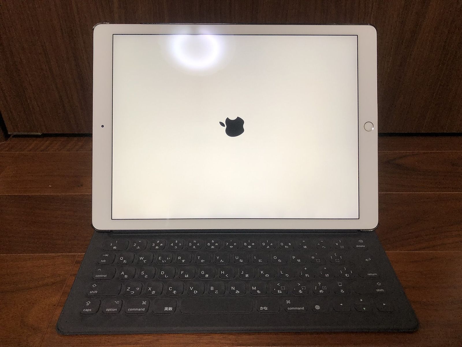 A silver 12.9-inch iPad Pro standing in a black Smart Keyboard with Japanese keys, its screen white with the Apple logo in the middle