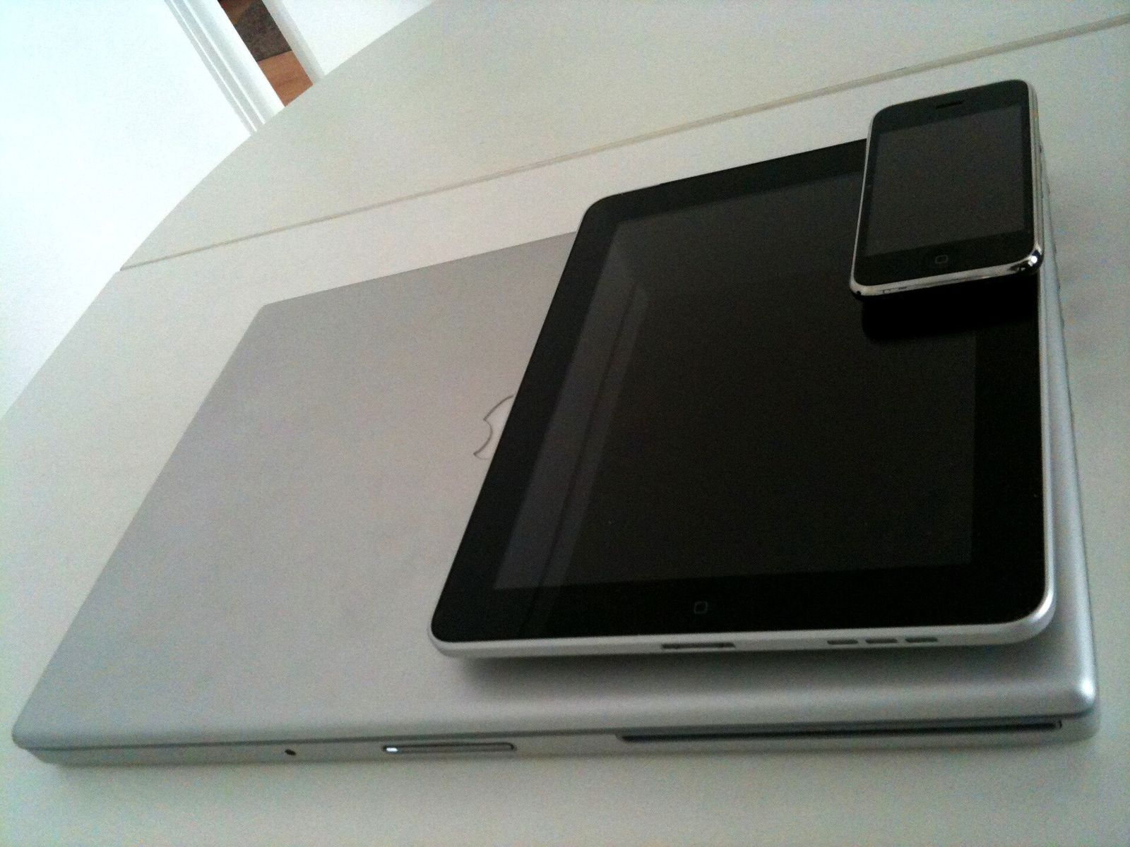 An iPhone resting on an iPad, which rests on a closed silver MacBook on a white table
