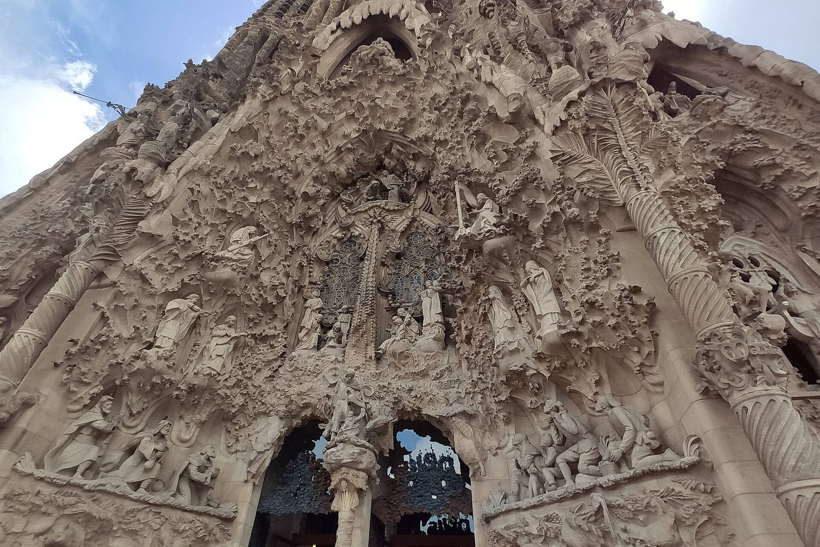 The Nativity façade of the Sagrada Família seen from below: a dense mass of carved figures, foliage and pinnacles around the central portal