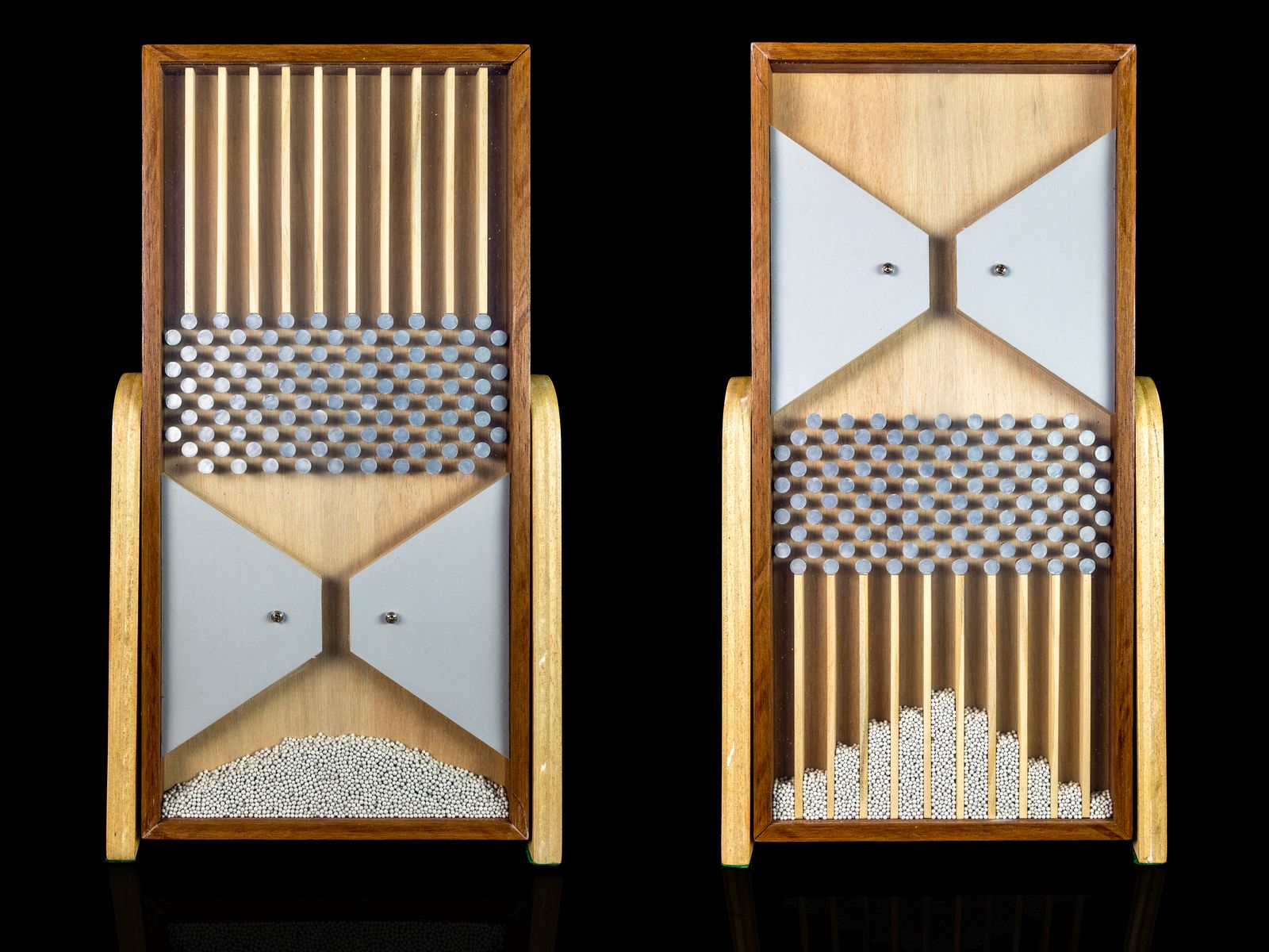 Two wooden Galton boards against a black background: in the left one the steel balls sit in a heap in the reservoir, and in the right one they have fallen through rows of pins into columns that form a bell shape