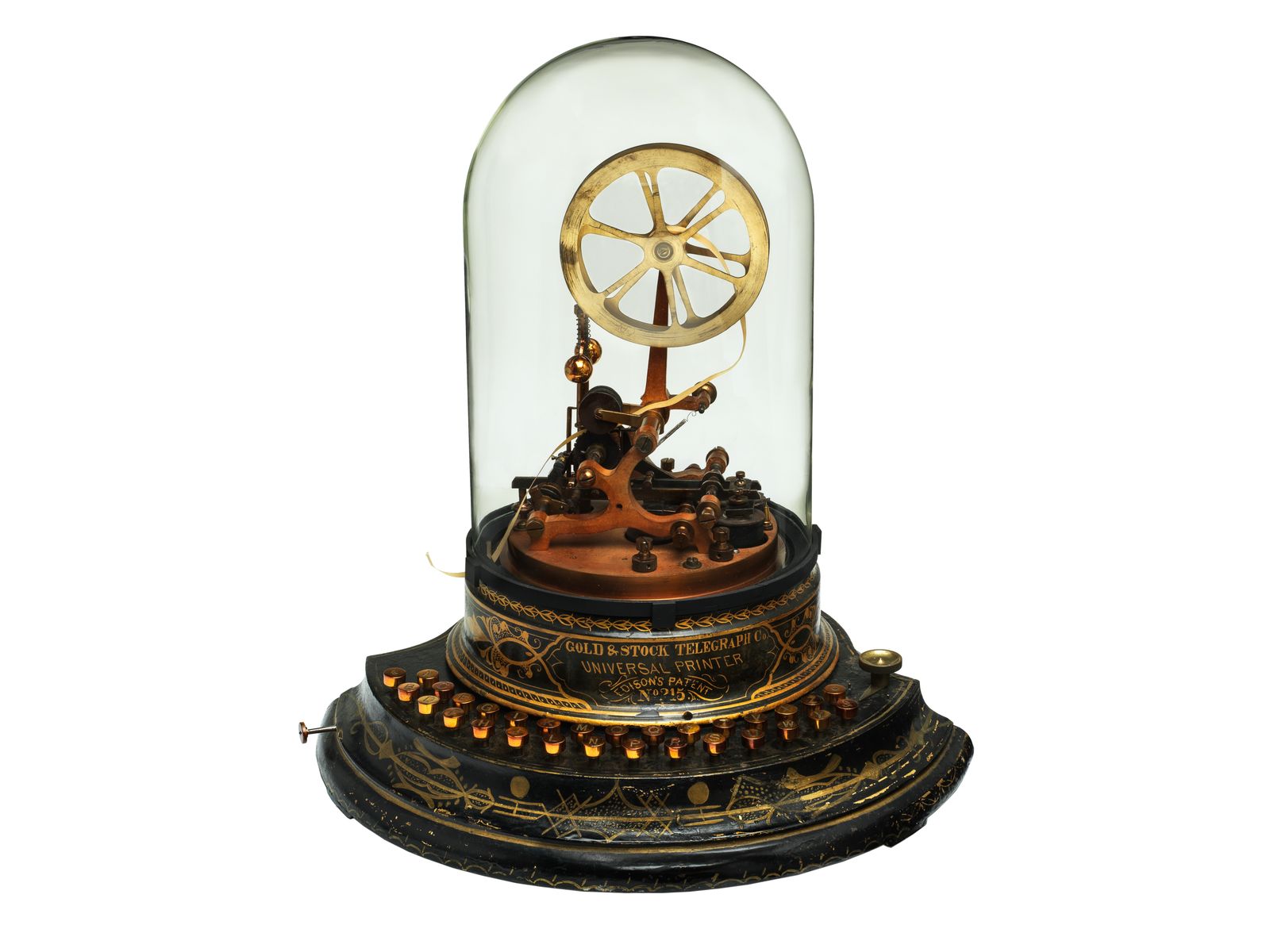 A brass and black stock ticker under a glass dome, with a wheel of paper tape at the top and a ring of small lettered keys around its base, which reads Gold and Stock Telegraph Co. Universal Printer