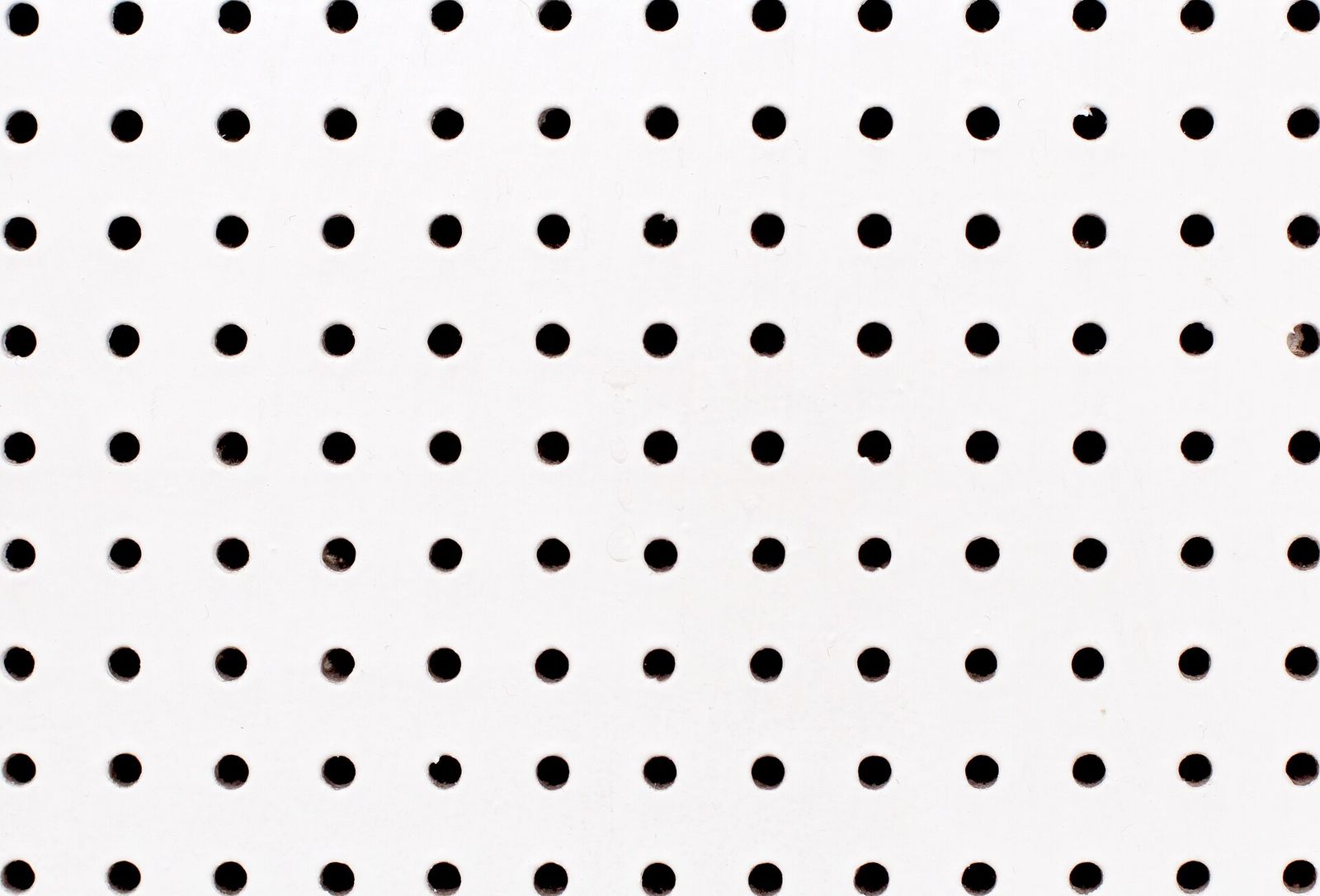 Rows of evenly spaced round black holes in a white-painted board