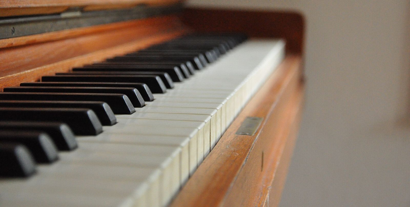 The black and white keys of a wooden upright piano, seen from one end with the far keys out of focus