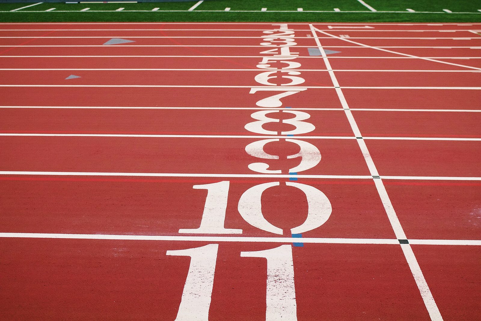 Close-up of a red running track at the start line, with white lane numbers 1 to 11 painted across the lanes