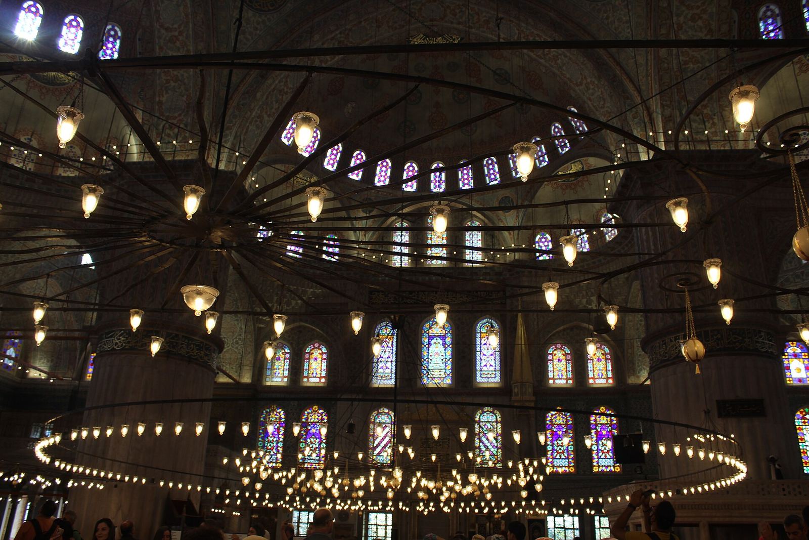 Inside the Blue Mosque: a ring of hanging lamps below rows of stained-glass windows and tiled arches