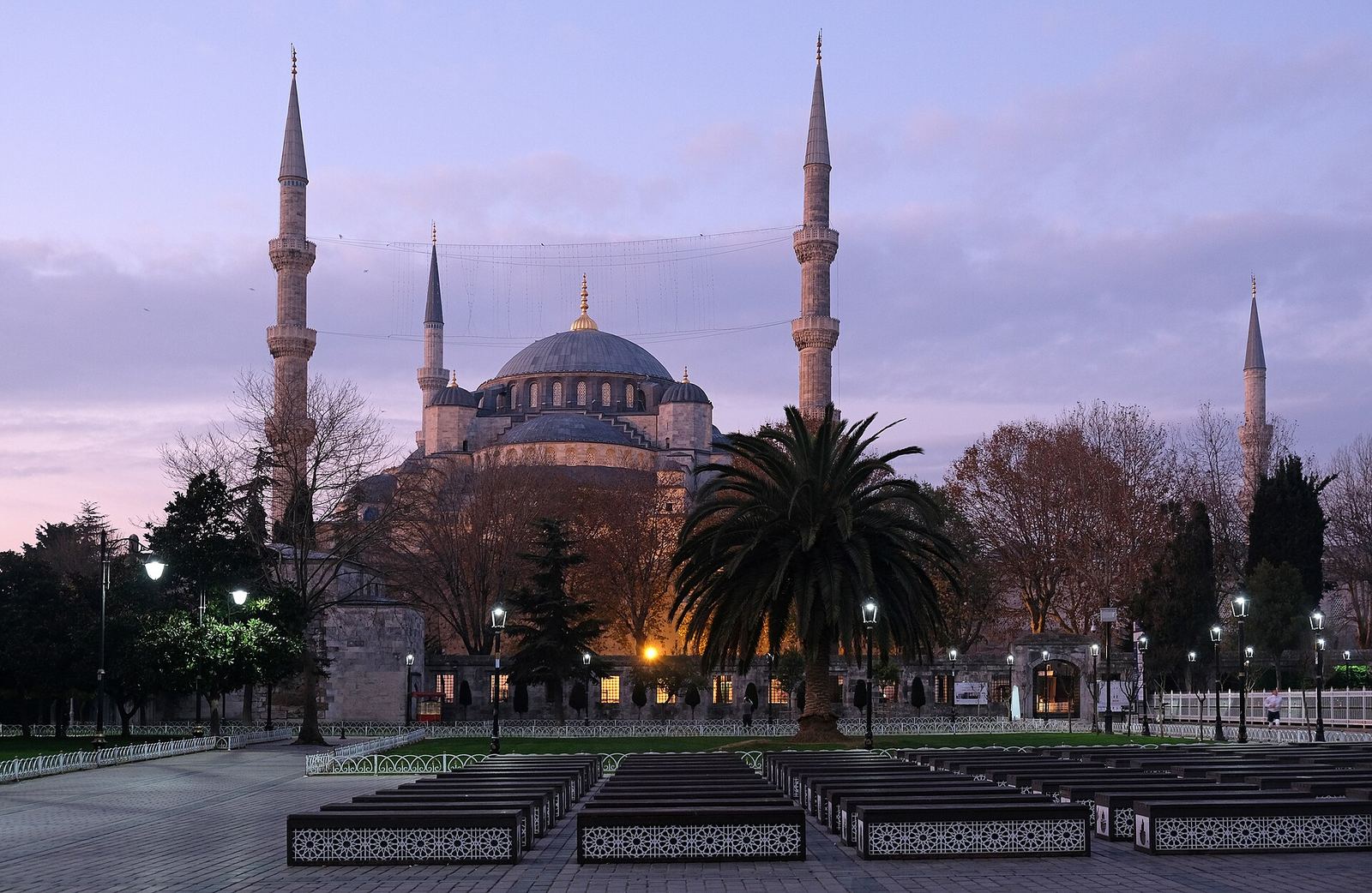 The Blue Mosque's domes and minarets seen across Sultanahmet Park at dusk, lamps lit along the paths