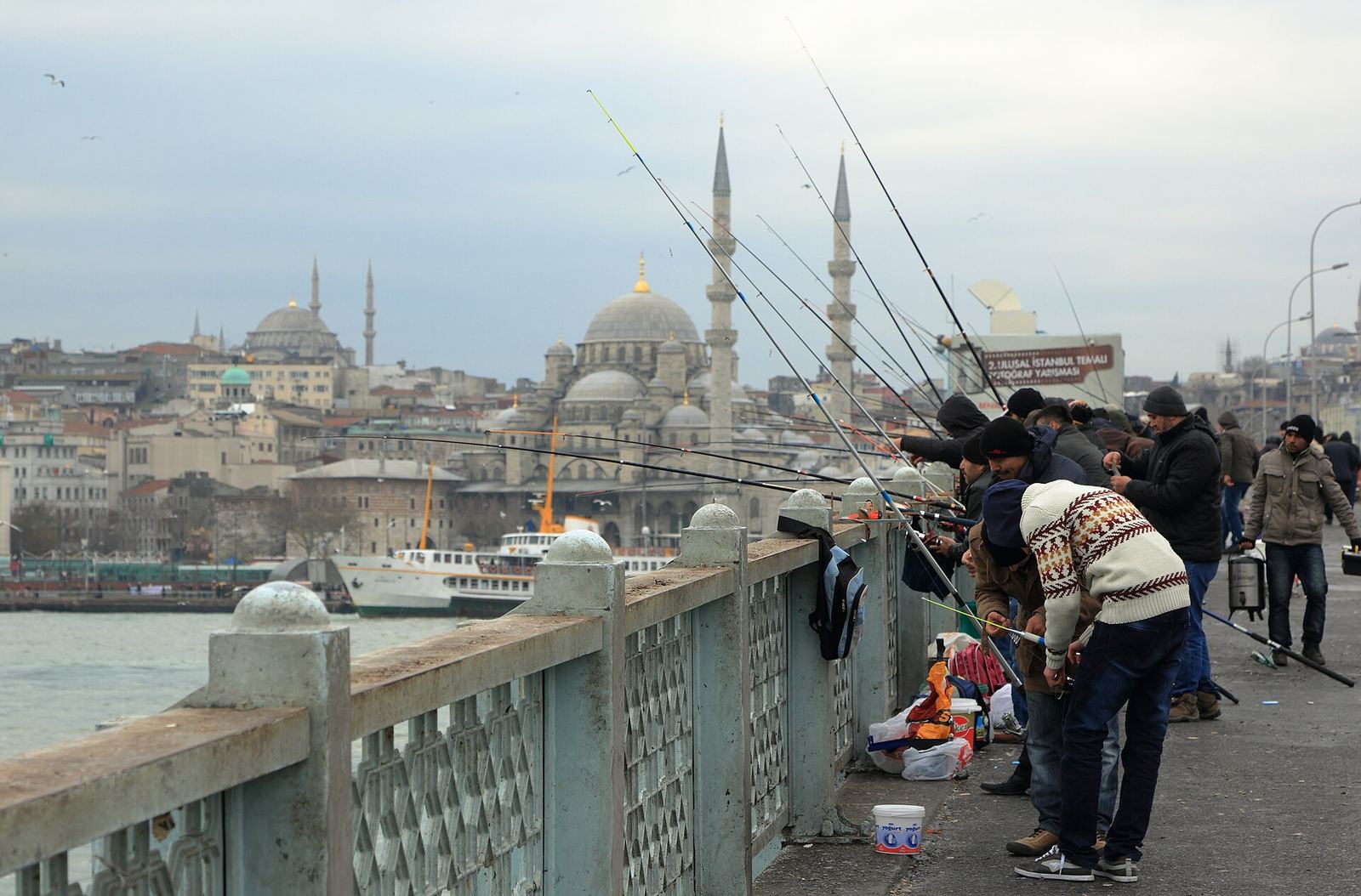 Anglers with long rods along the Galata Bridge railing, the New Mosque and Süleymaniye on the skyline behind