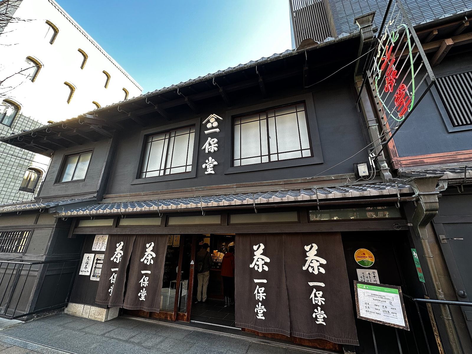 The dark wooden two-storey front of Ippodo Tea's main shop, with white-lettered noren curtains over the entrance and a large signboard on the roof