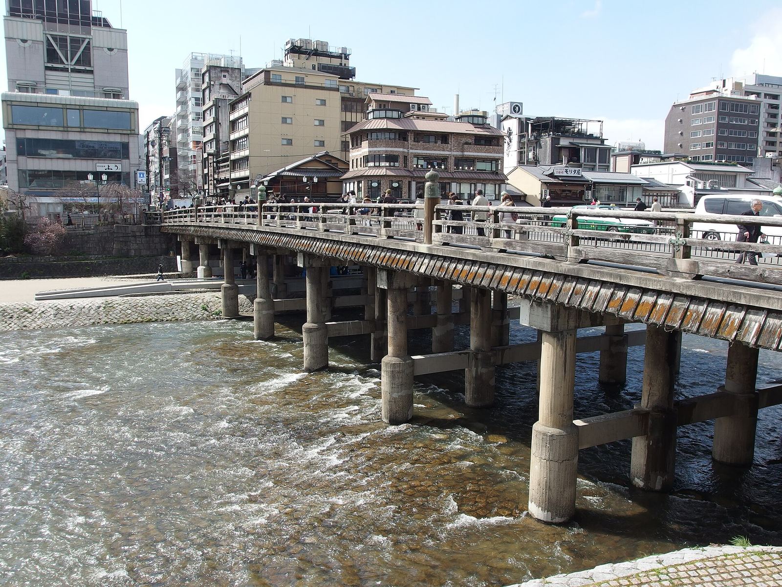 The long, low Sanjo Ohashi bridge crossing the shallow Kamo River, with downtown buildings behind it on a clear day