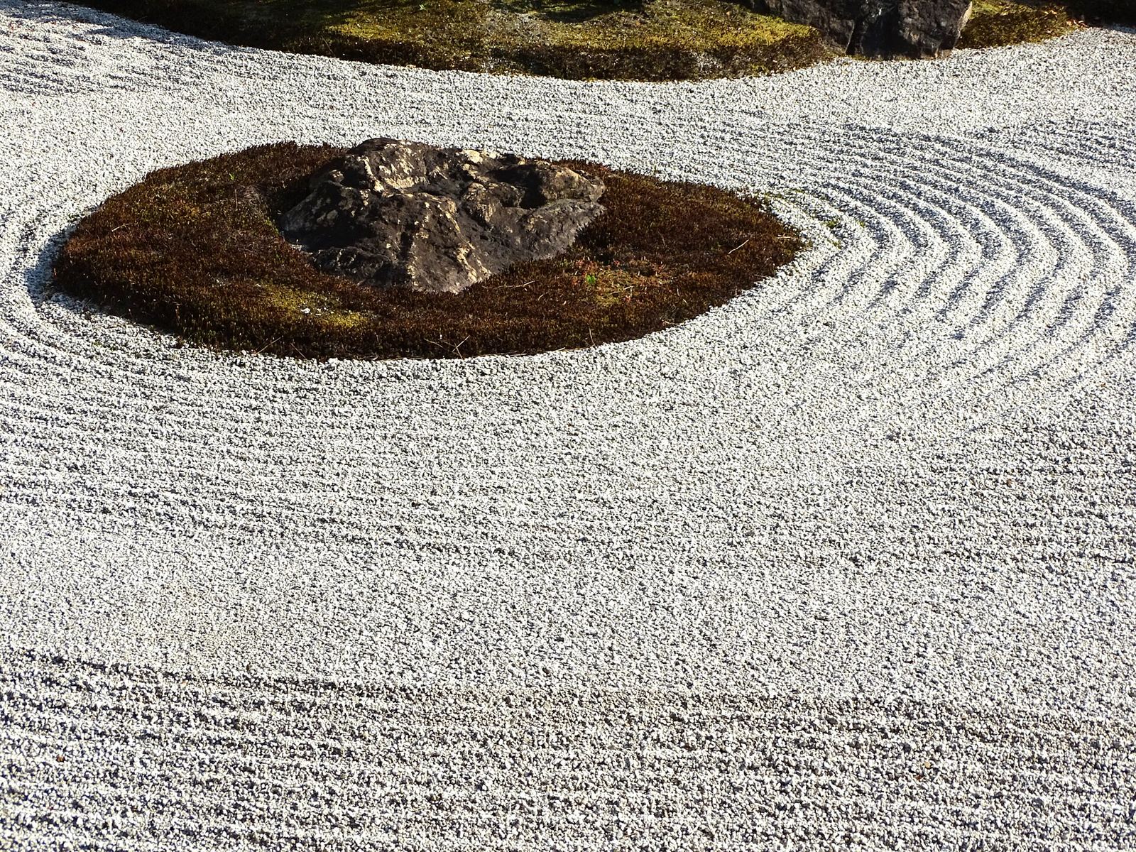 Raked white gravel swirling around a low mound of moss and a single rock in the dry garden at Kennin-ji