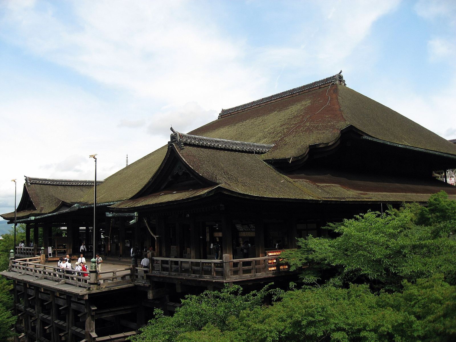 The Main Hall of Kiyomizu-dera and its wooden stage raised on tall pillars among green trees, with the city and hills beyond