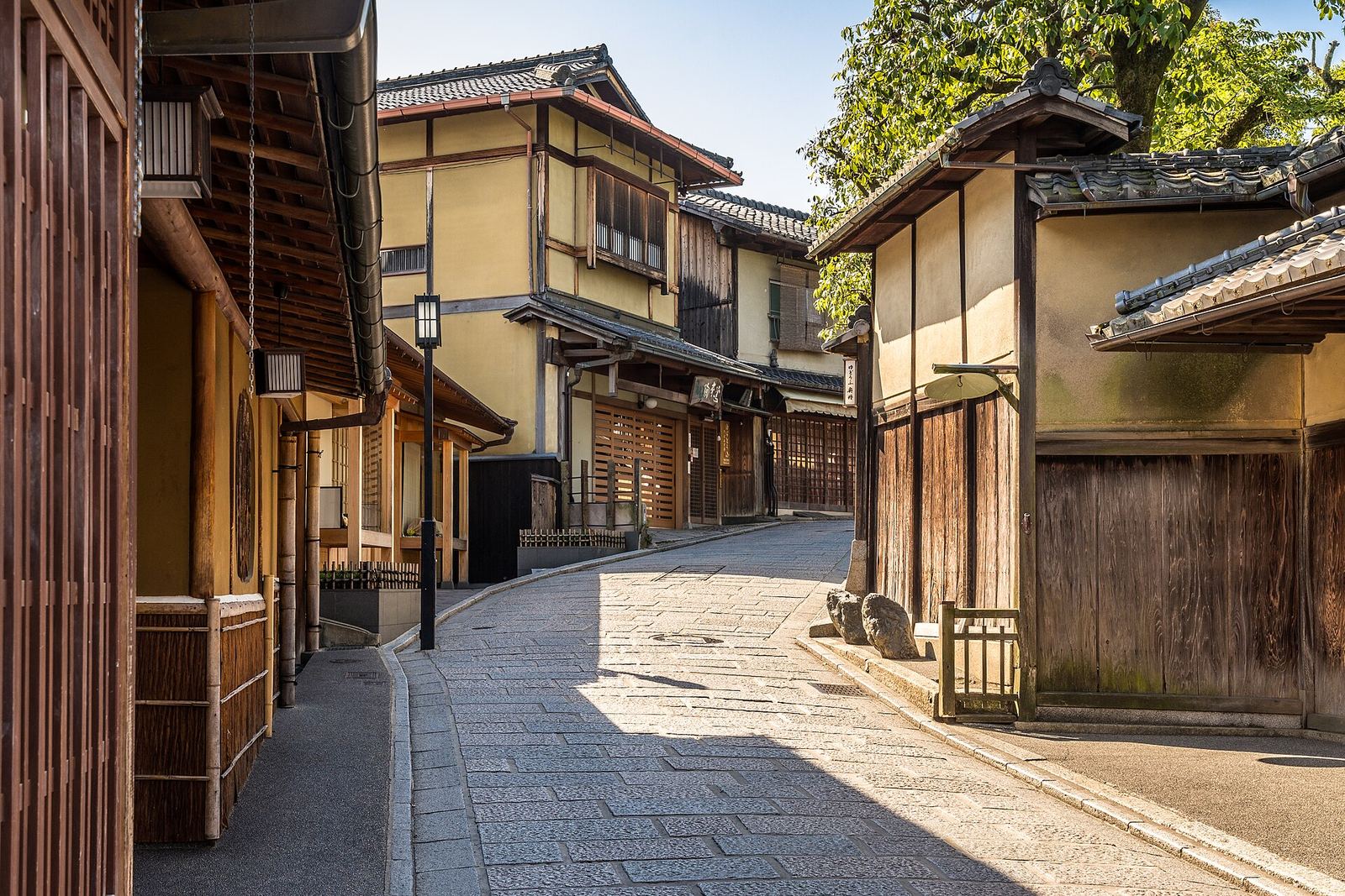 Ninenzaka's empty stone-paved lane curving between two-storey wooden shopfronts with tiled roofs, in bright sun