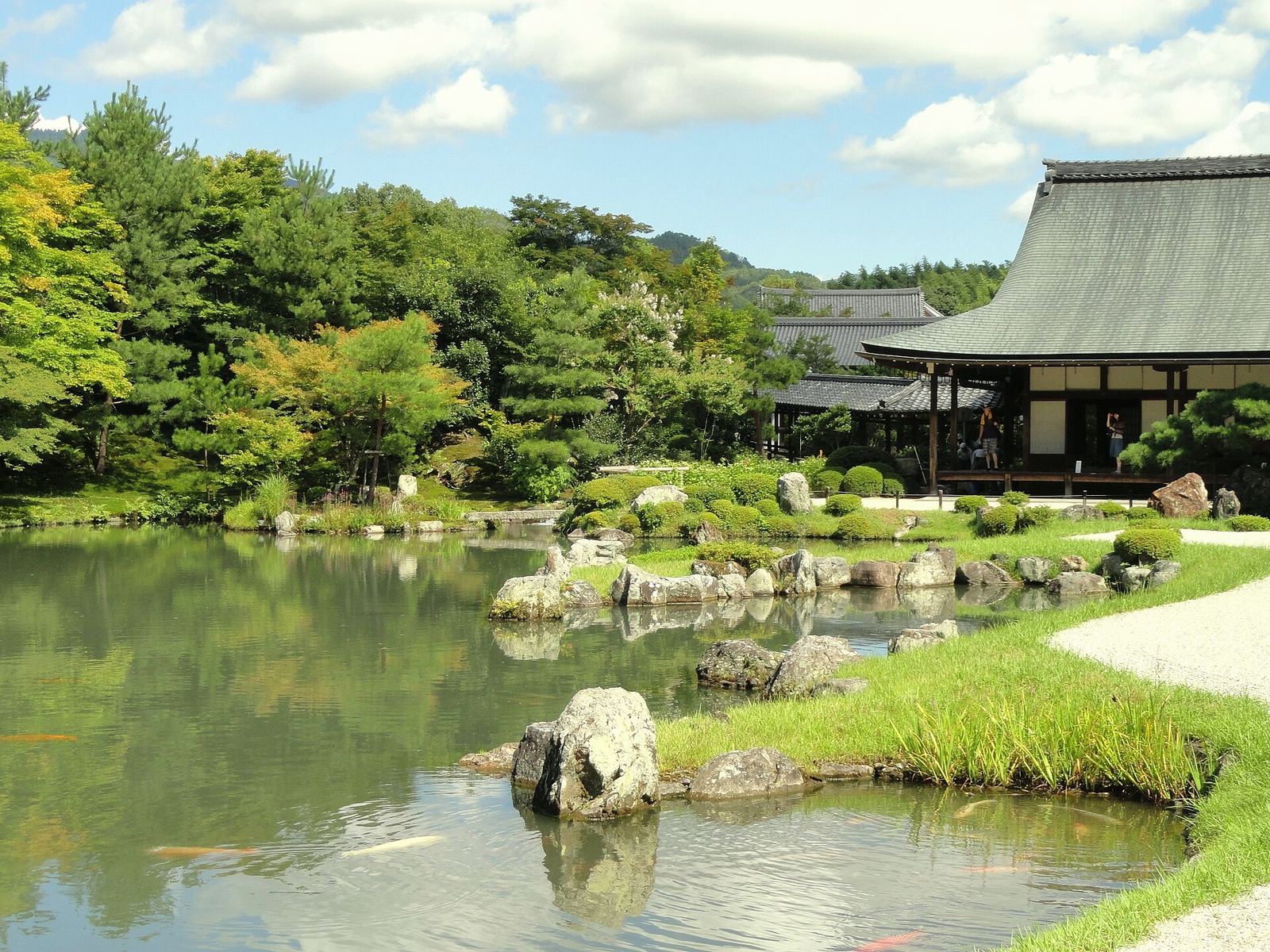Tenryu-ji's Sogenchi pond reflecting green trees and rocks, with the temple's long, low abbot's hall on the right bank