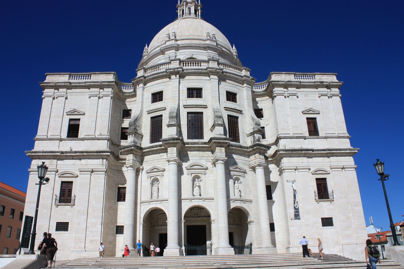 The white stone facade and dome of the Panteão Nacional against a deep blue sky, with a wide stairway leading up to its three arched doors
