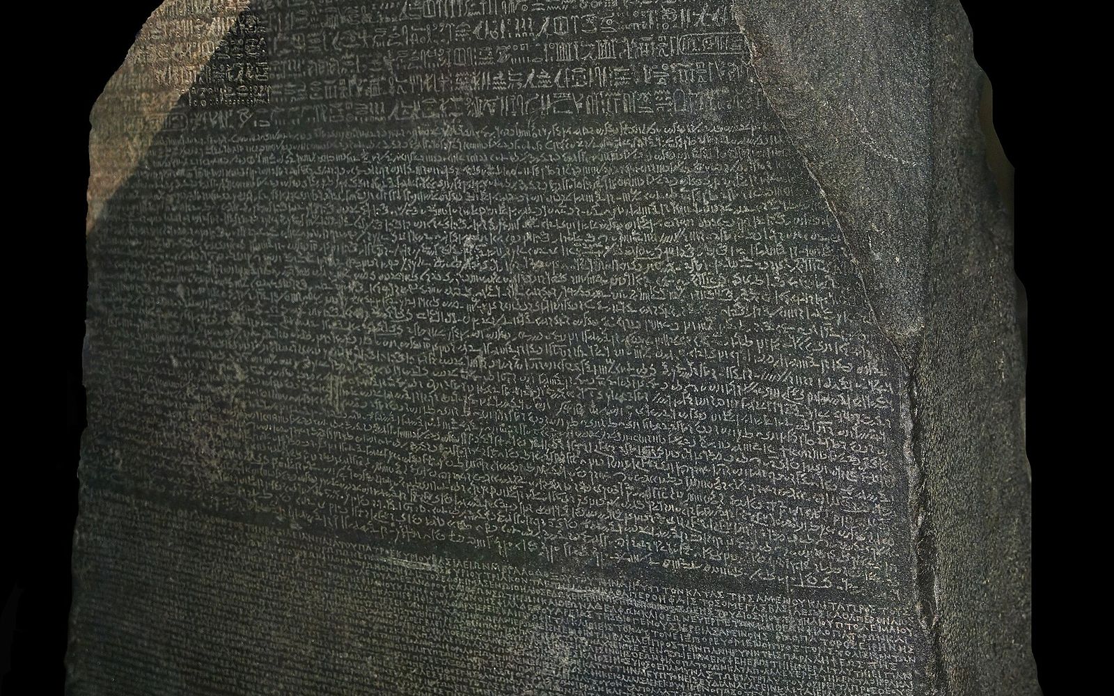 Close view of the Rosetta Stone's dark face, with rows of hieroglyphs at the top, dense Demotic script across the middle and Greek letters along the bottom