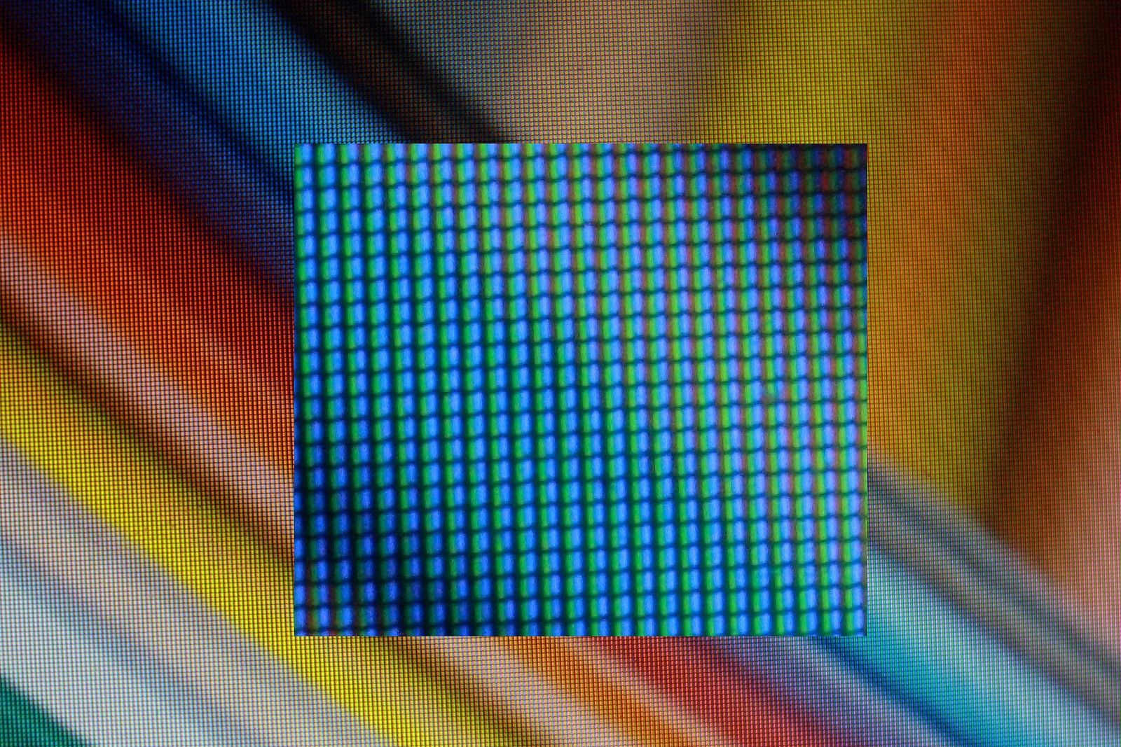 Macro photo of a laptop screen showing a rainbow gradient as a fine grid of coloured subpixels, with a more magnified inset in the centre showing columns of blue and green subpixels