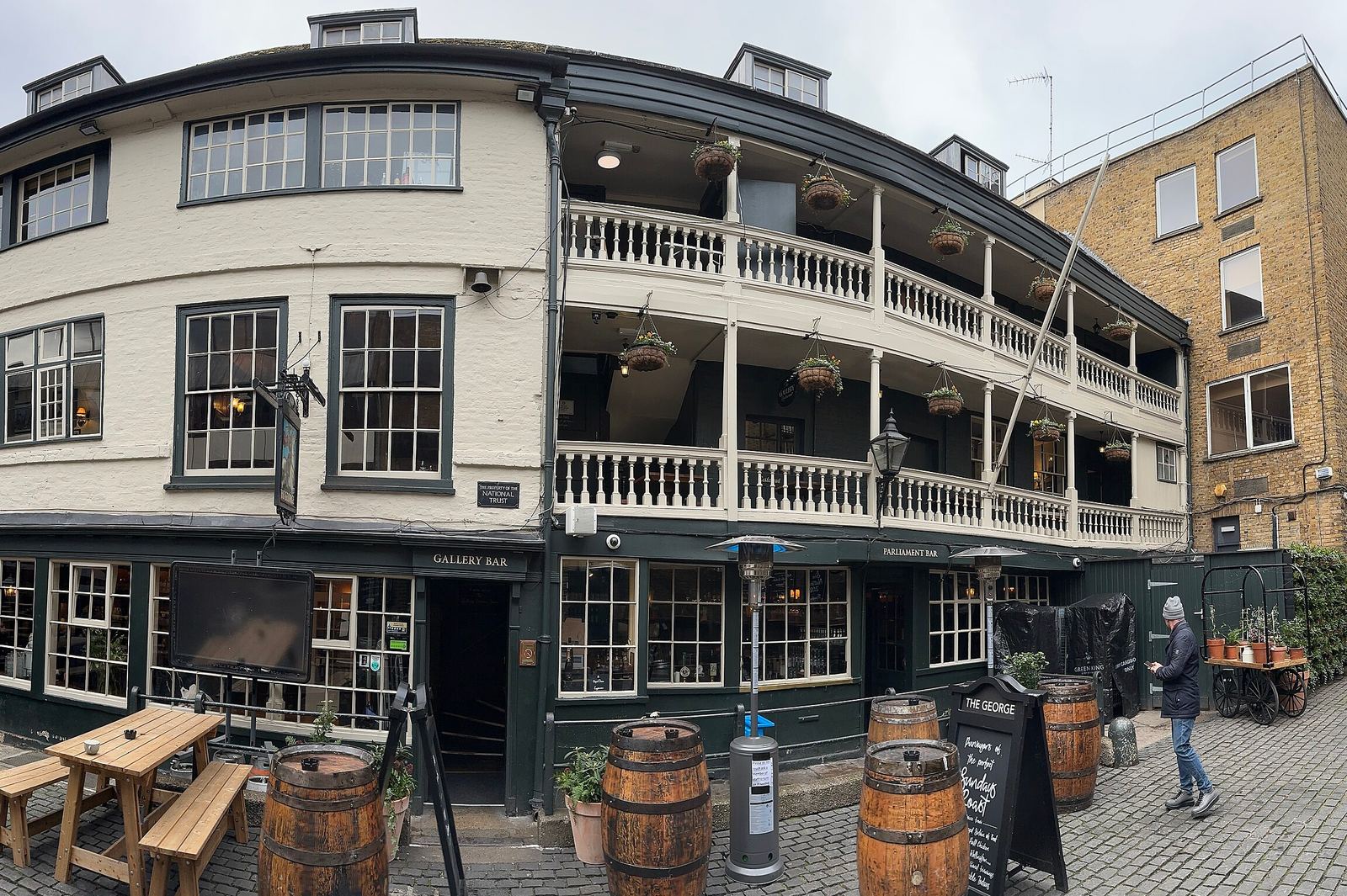The George Inn in Southwark: a white-painted building with two tiers of wooden galleries and hanging flower baskets above a cobbled courtyard with barrels and benches