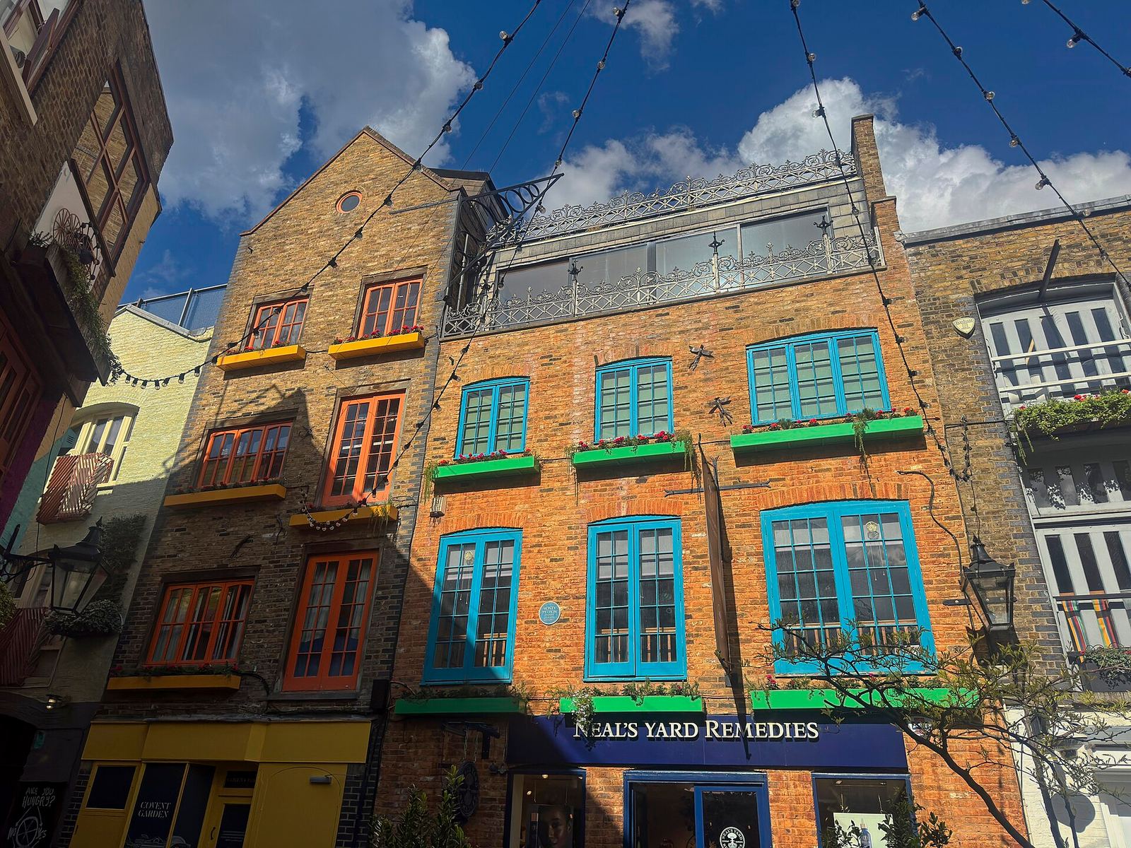 Neal's Yard in Covent Garden: old brick buildings with window frames painted bright blue, orange and green, and strings of lights across a blue sky
