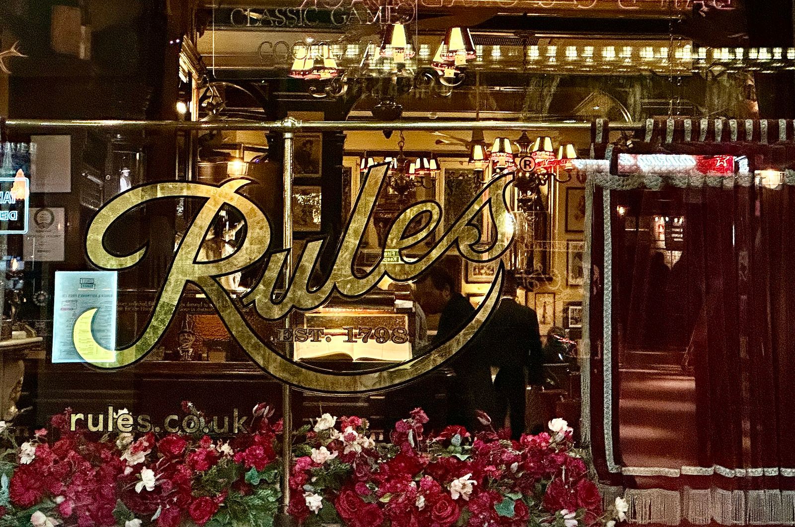 The window of Rules at dusk, with RULES EST. 1798 in gold script on the glass and a glimpse of the red, gilded dining room behind