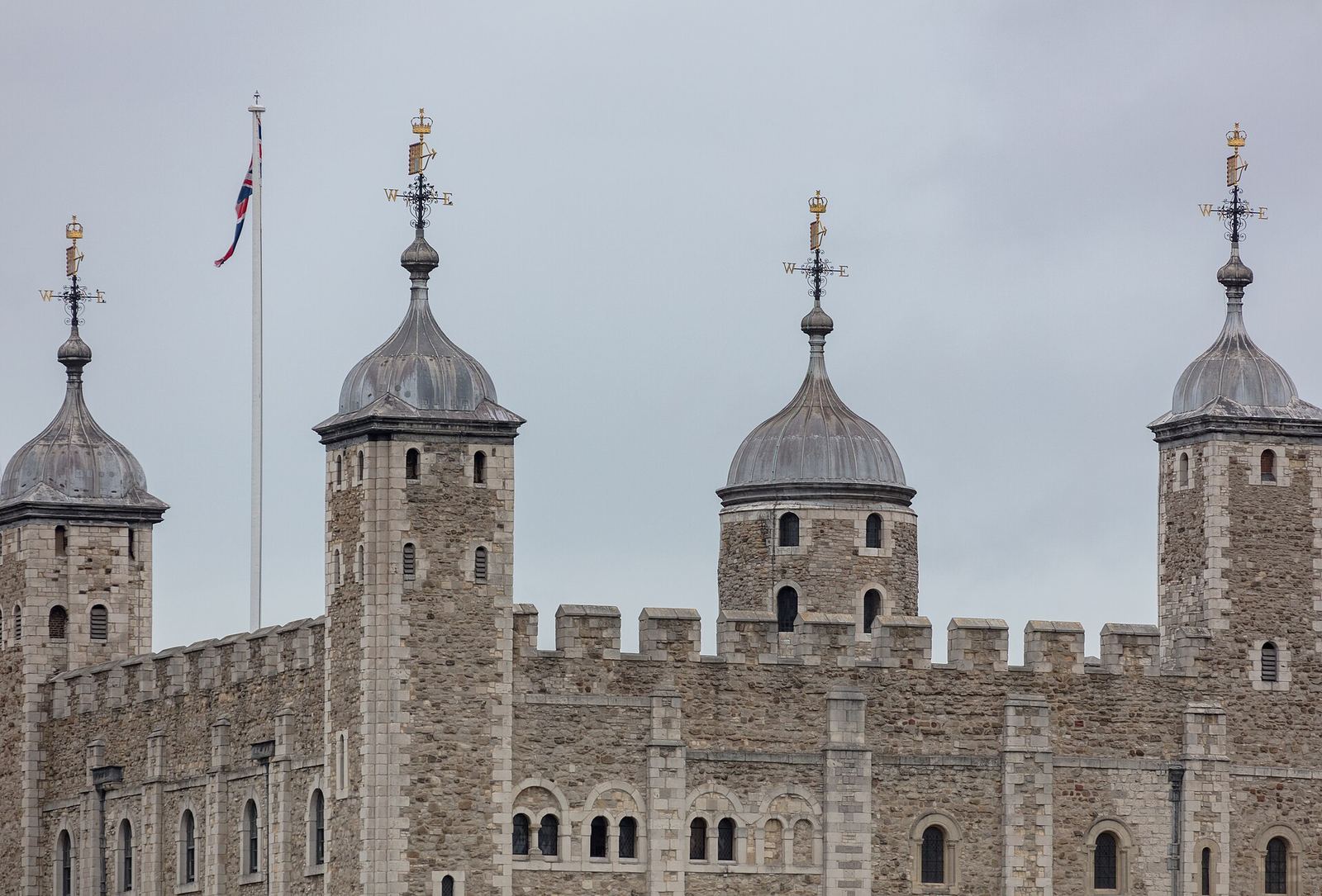 The White Tower at the Tower of London: pale stone walls and battlements with four corner turrets topped by lead cupolas and weathervanes, a Union flag flying above