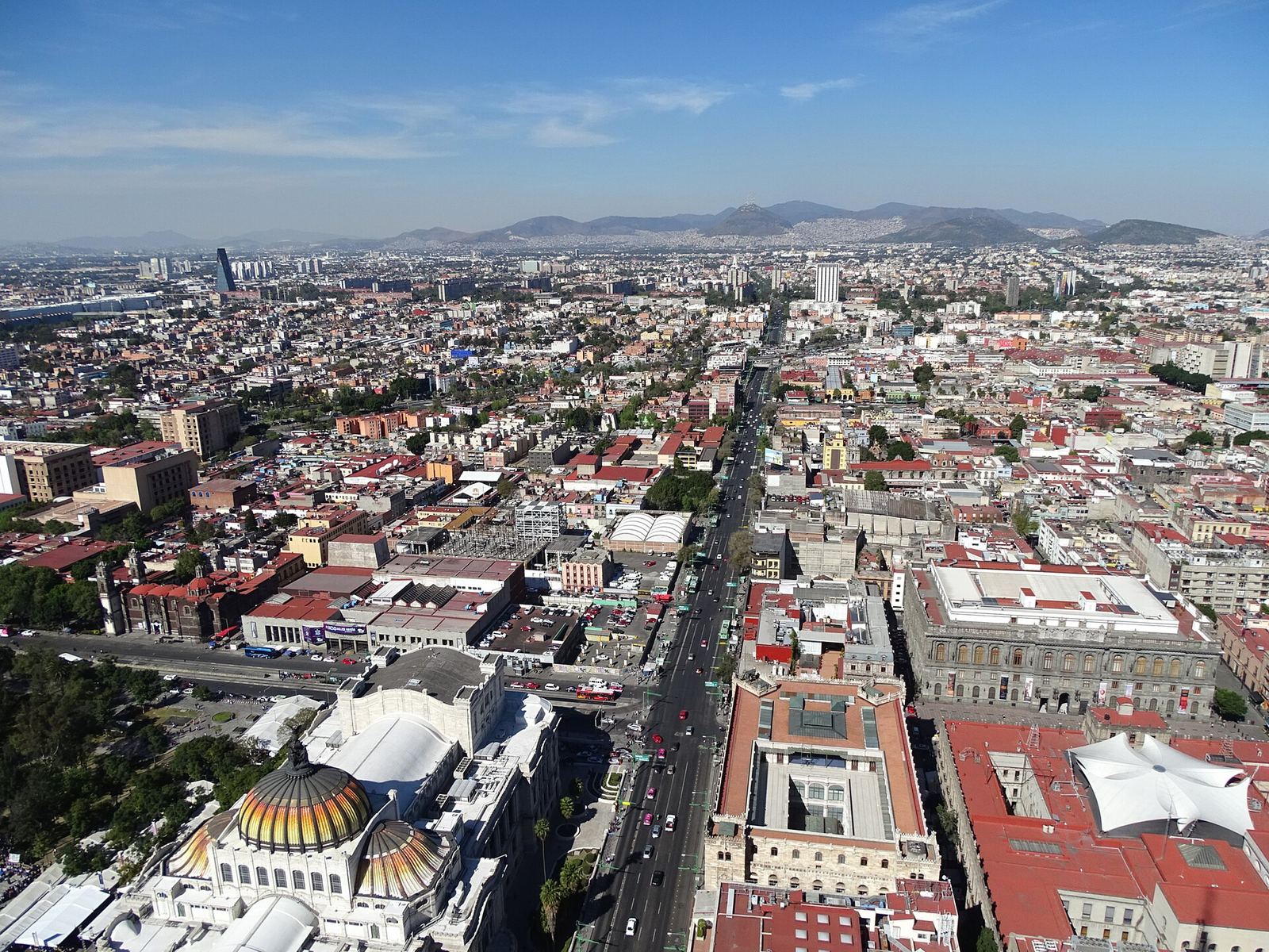The view west from the top of the Torre Latinoamericana: the domes of the Palacio de Bellas Artes at the bottom, Avenida Juárez and the Alameda, and the city stretching to the mountains under a blue sky