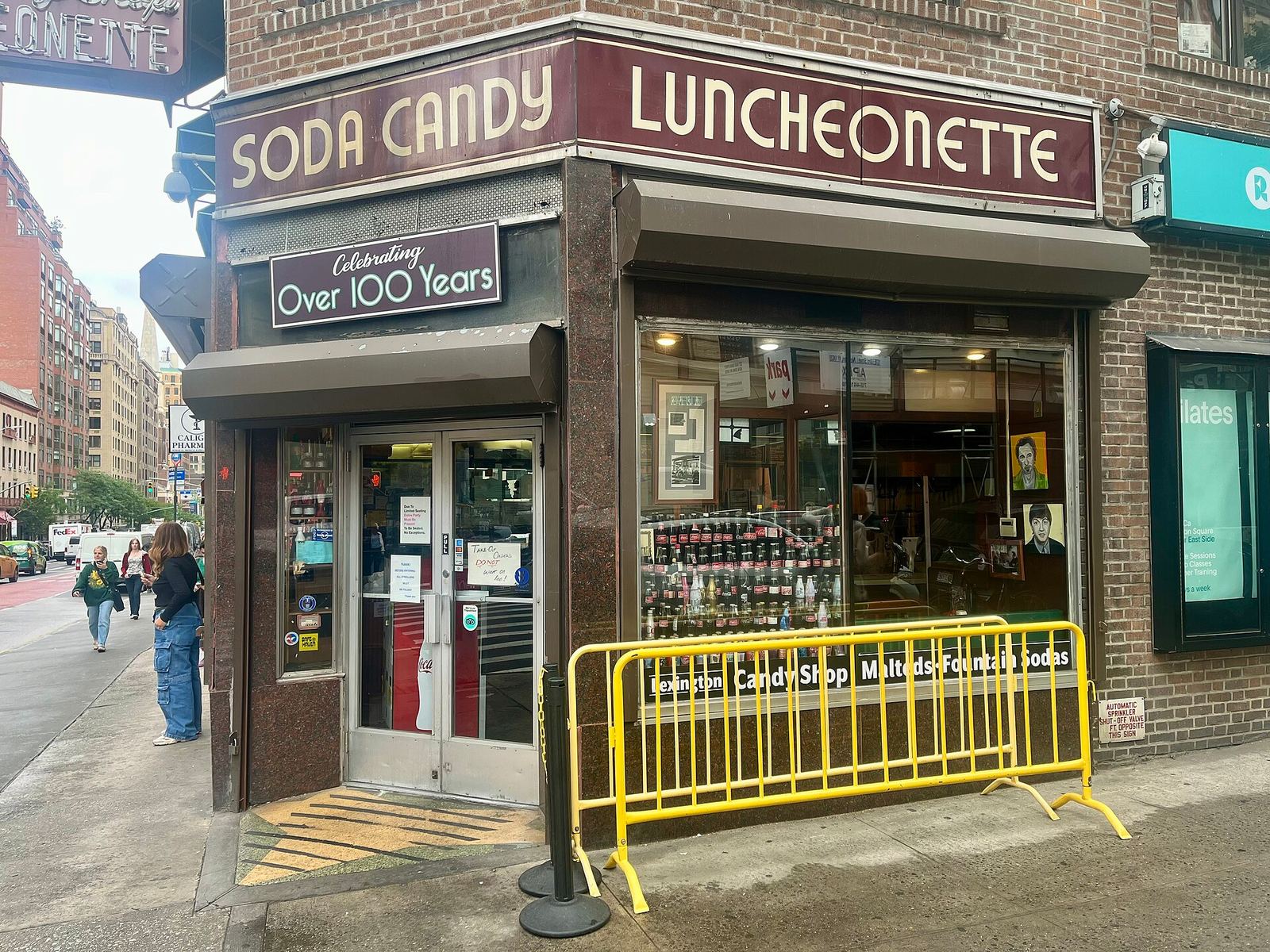 The corner storefront of Lexington Candy Shop, with its 'Soda Candy Luncheonette' sign and a smaller 'Celebrating Over 100 Years' sign above the door