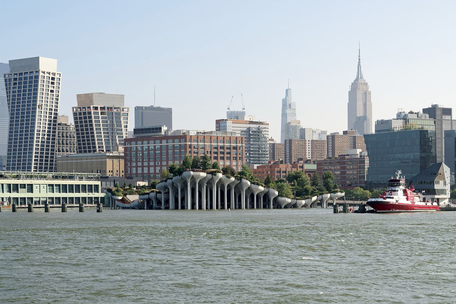 Little Island seen from the Hudson River: the park's undulating platform on dozens of tulip-shaped concrete piers, with Chelsea's buildings and the Empire State Building behind