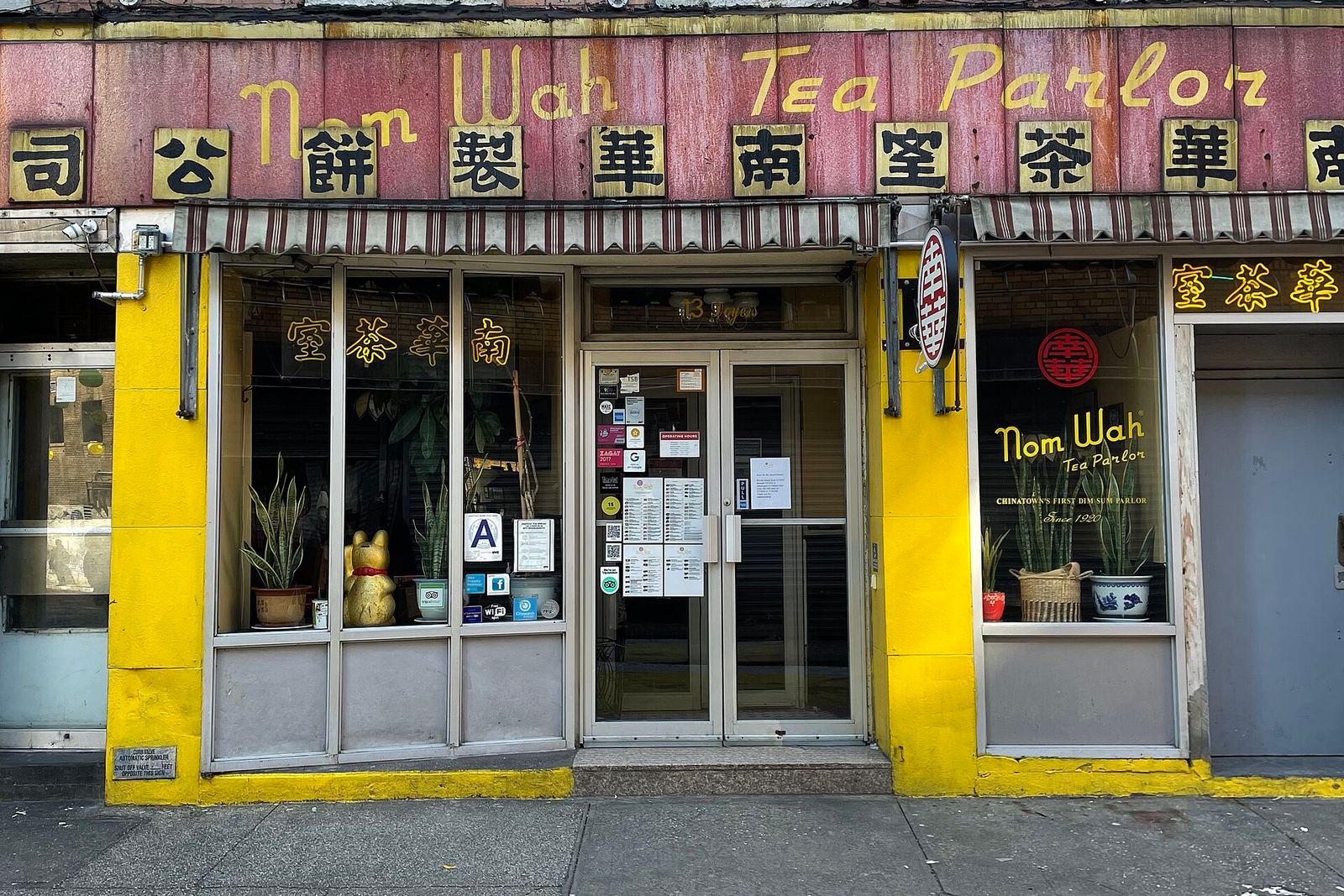 The Nom Wah Tea Parlor storefront on Doyers Street: a faded red sign with the name in gold script and Chinese characters above yellow-framed windows and glass doors
