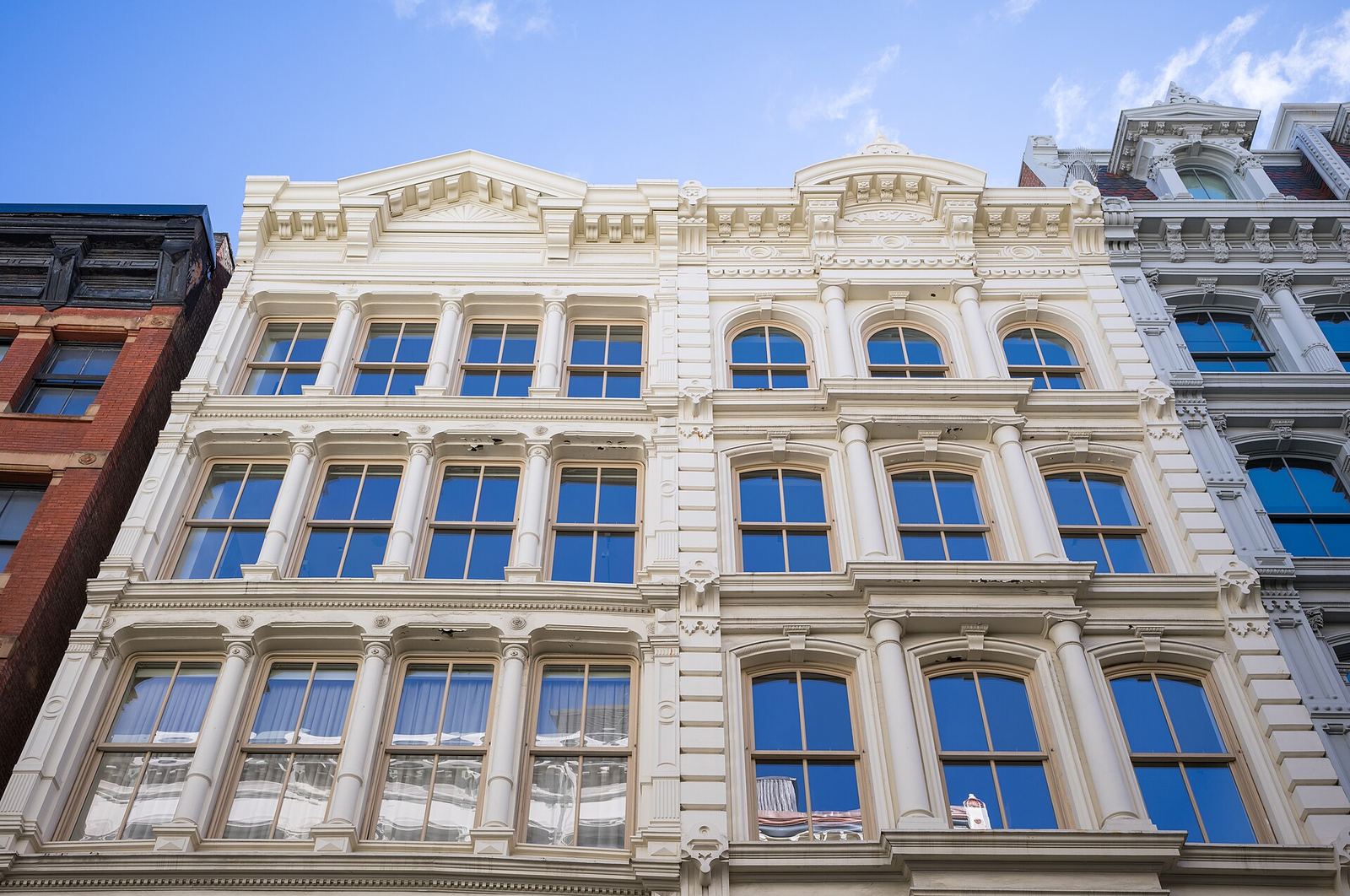 The cream-painted cast-iron facade of 28 Greene Street in SoHo, rows of arched windows between slim columns rising to a mansard roof against a blue sky