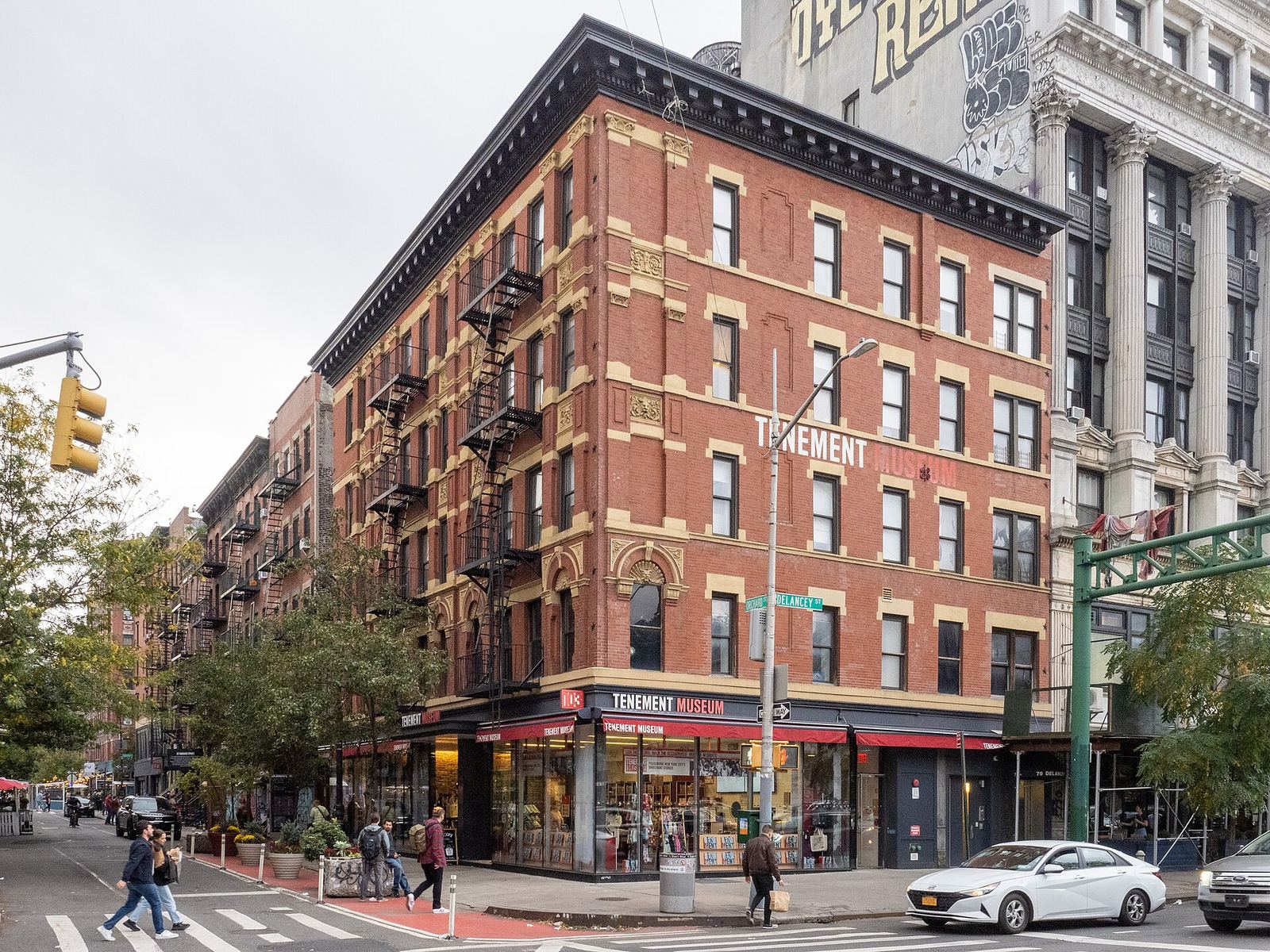 The Tenement Museum's red-brick building on the corner of Orchard and Delancey Streets, with fire escapes on the facade and the museum shop at street level