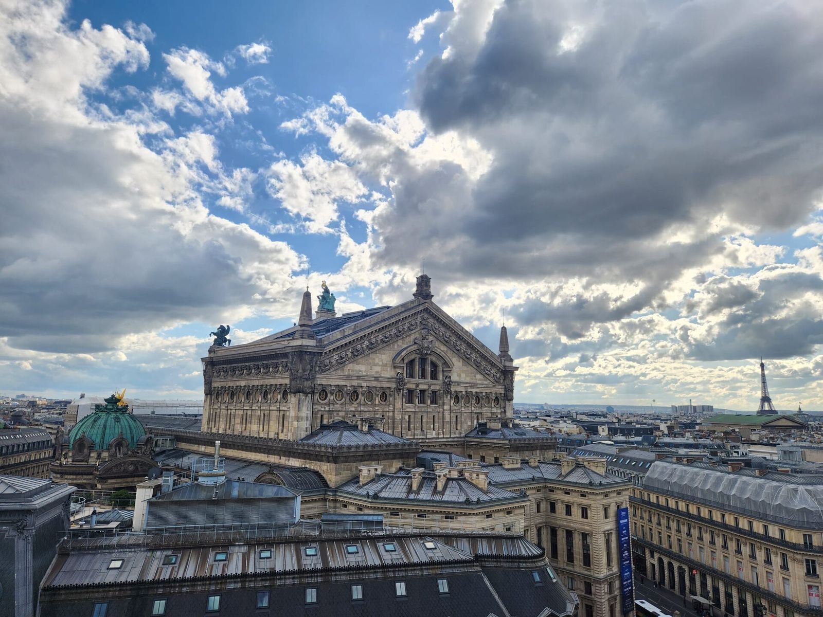 The view from the Galeries Lafayette rooftop terrace: the Opéra Garnier's roof and green dome in front, the Eiffel Tower on the horizon, under big clouds