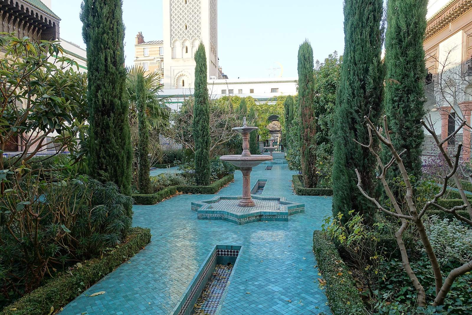 The garden of the Grande Mosquée de Paris: a tiled fountain and turquoise water channel between clipped hedges and cypresses, with the square minaret rising behind