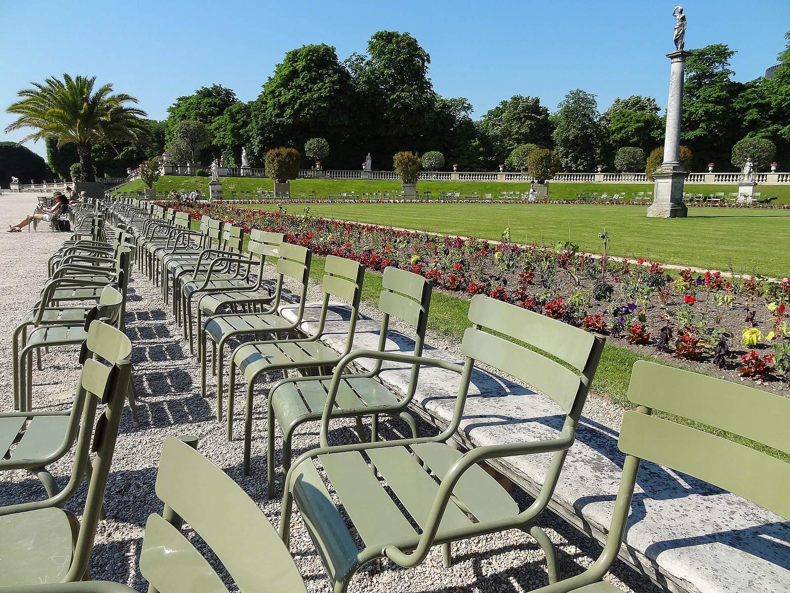 Rows of the Jardin du Luxembourg's green metal chairs set out on the gravel beside flower beds and lawns on a sunny day