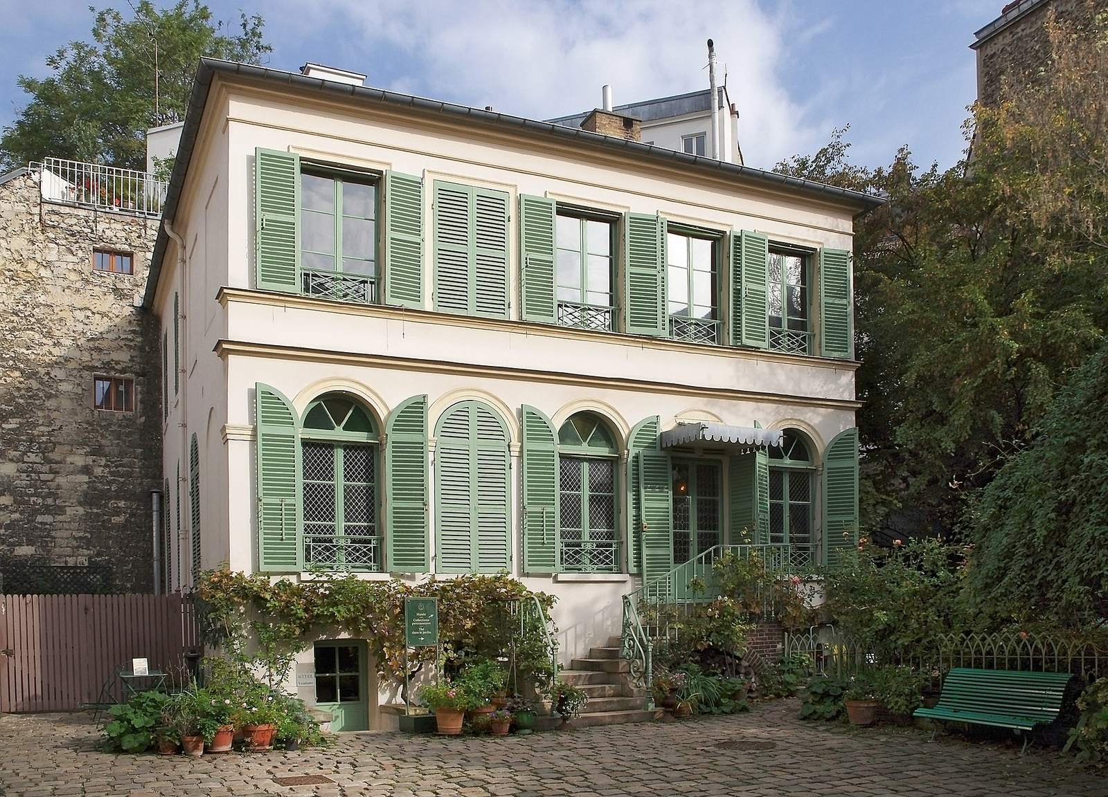 The Musée de la Vie Romantique: a cream-coloured townhouse with pale green shutters behind a cobbled courtyard with potted plants and a green bench
