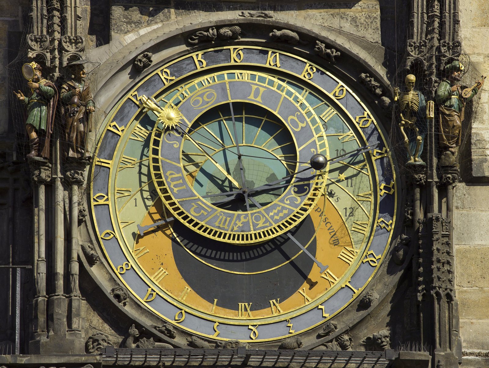 The blue and gold astronomical dial of the Prague Orloj, with its zodiac ring and sun and moon hands, framed by carved Gothic stonework and figures