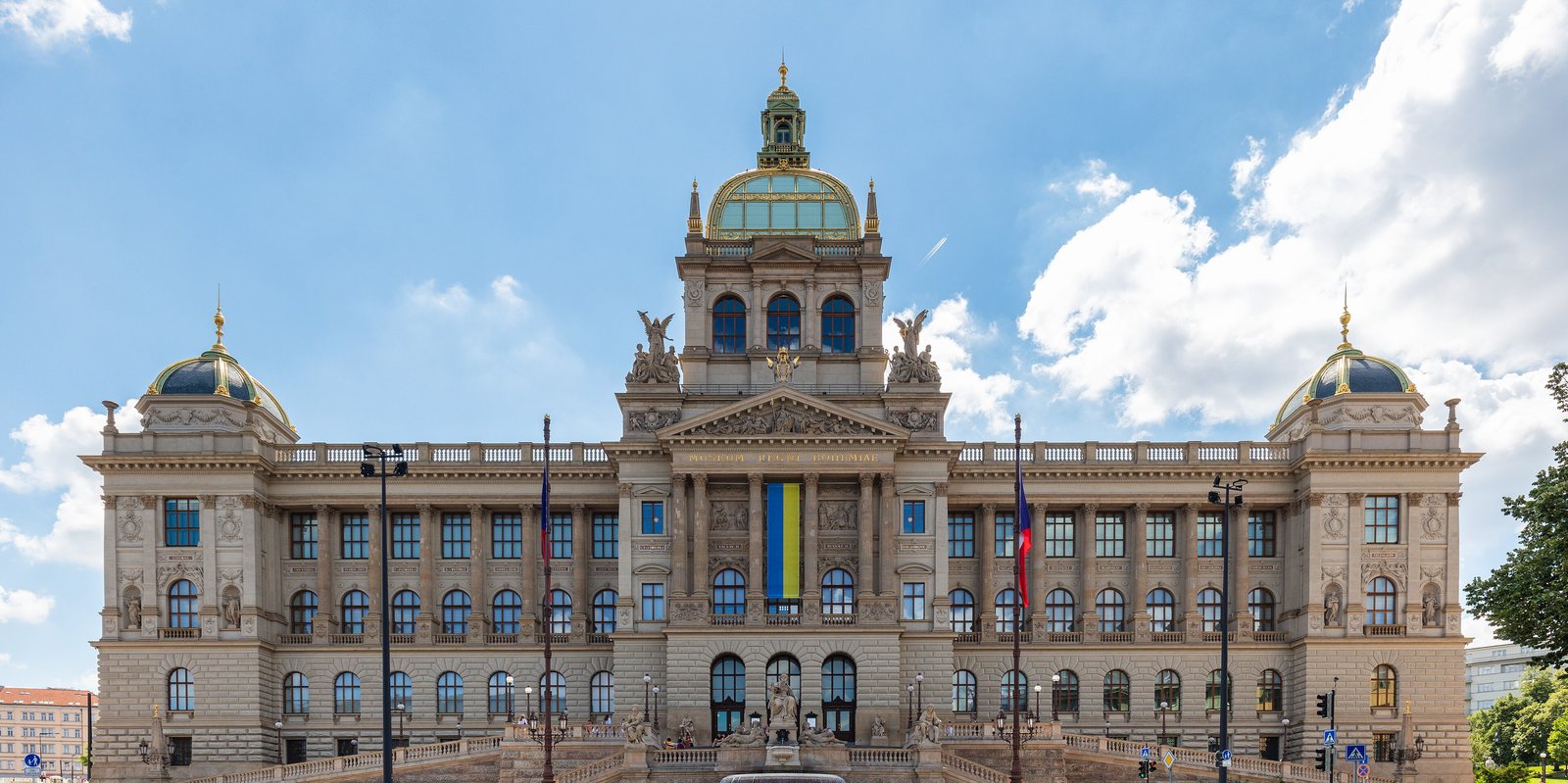 The Historical Building of the National Museum at the top of Wenceslas Square: a long Neo-Renaissance facade with a central dome and corner cupolas, and a blue and yellow banner over the entrance