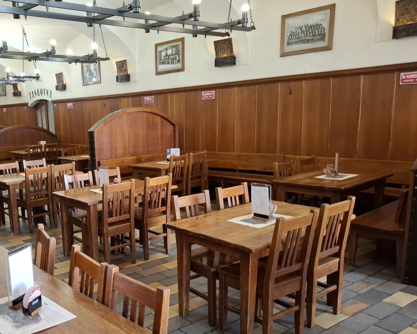 U Medvídků's beer hall: wooden tables and chairs, wood-panelled walls and iron chandeliers under a white vaulted ceiling, with a sign reading Tankovna