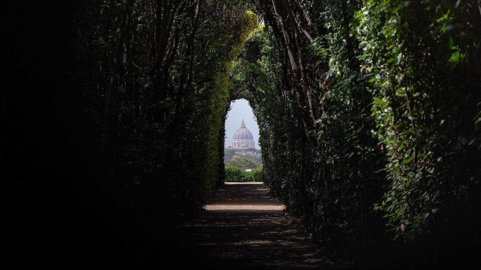 The view through the Knights of Malta keyhole: a gravel path running through a dark tunnel of hedges, with the dome of St Peter's framed at the far end