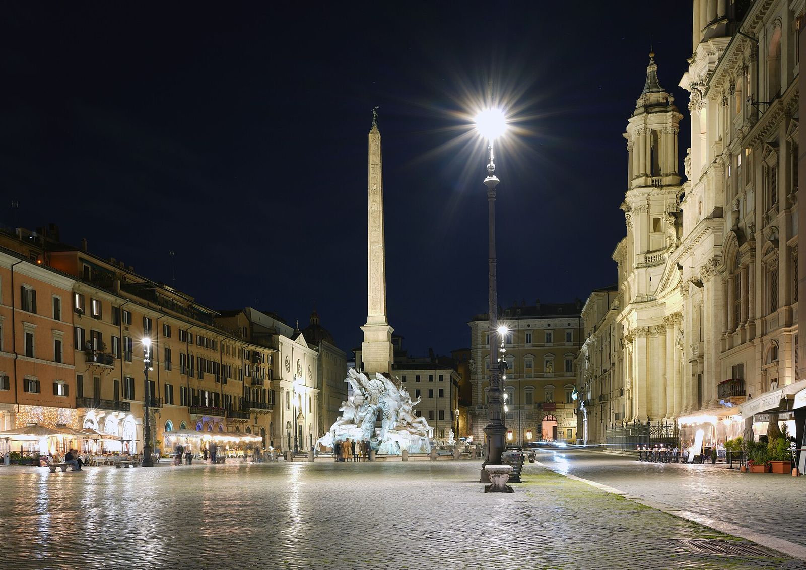 Piazza Navona at night: Bernini's Fountain of the Four Rivers and its obelisk lit up on the wet cobbles, with the front of Sant'Agnese in Agone on the right