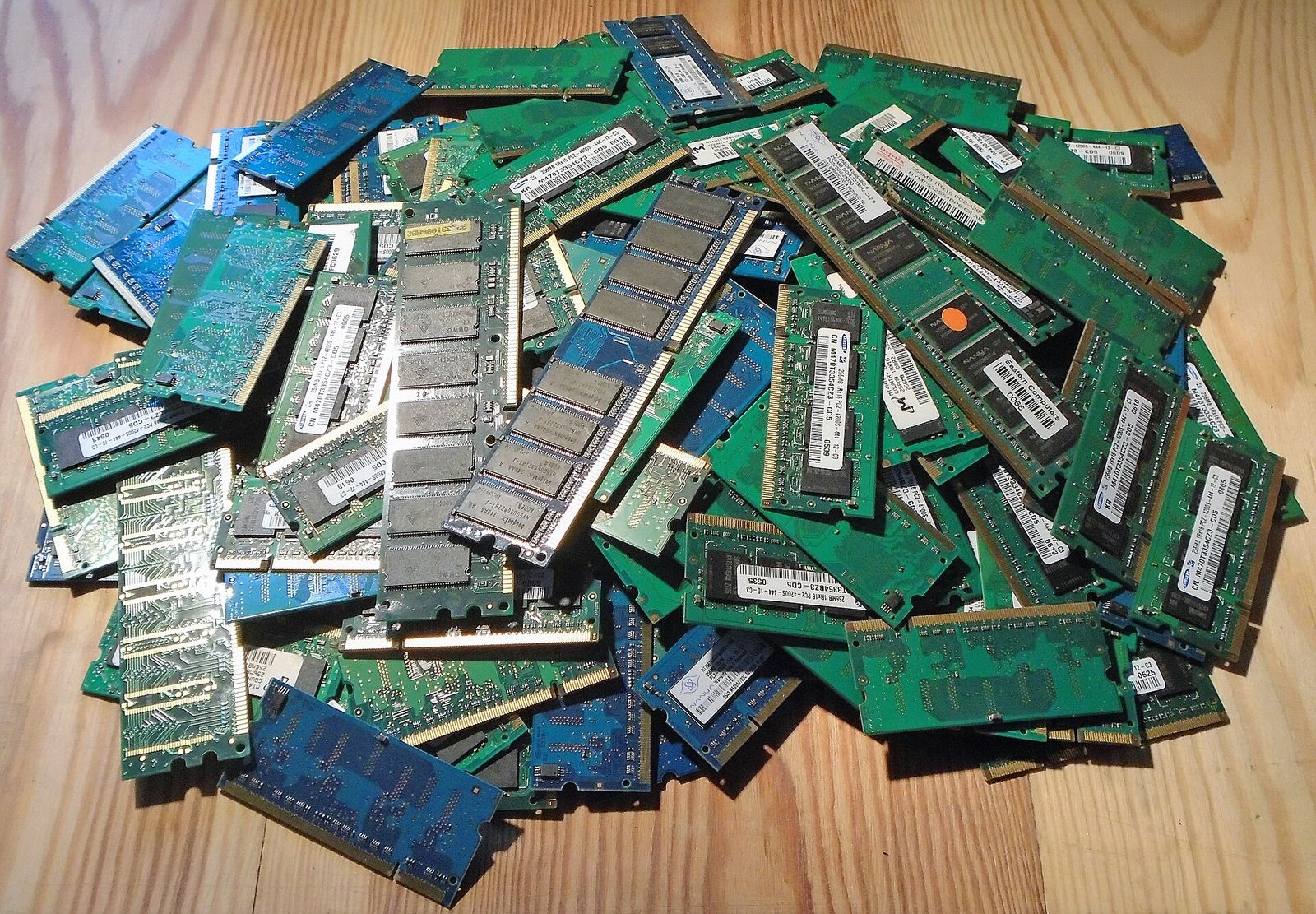 A heap of green and blue laptop and desktop memory modules on a wooden table