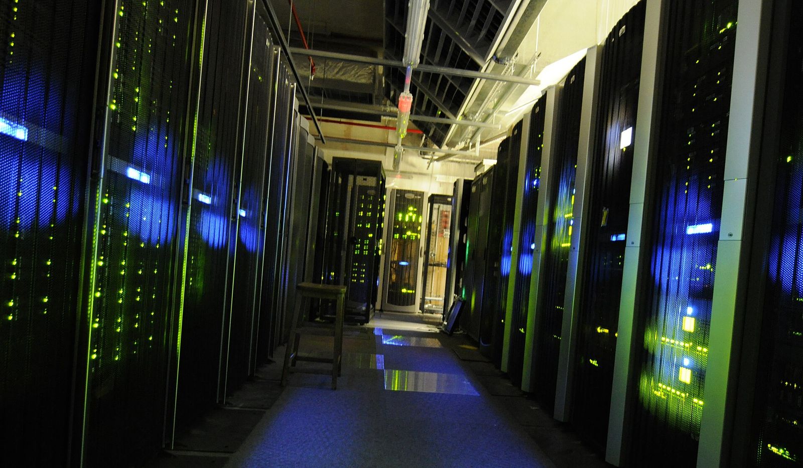 A dim aisle between rows of black server racks lit by green and blue status lights