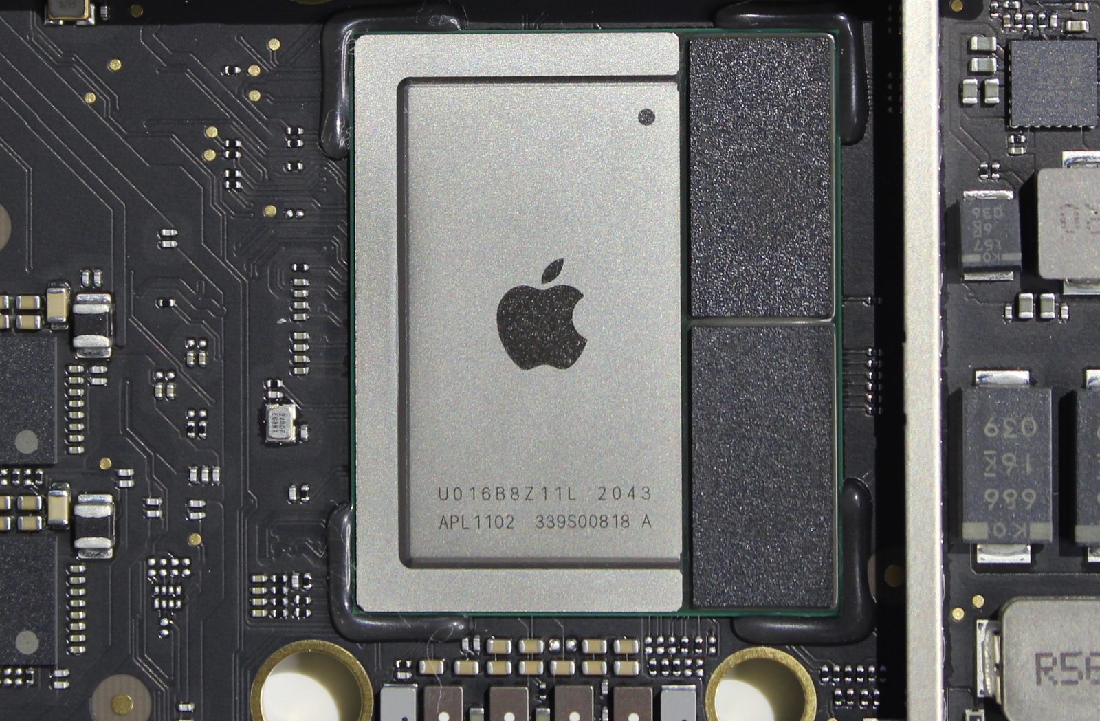 Apple's M1 chip on a Mac mini logic board: a silver lid with the Apple logo and part numbers, and two dark memory chips beside it in the same package