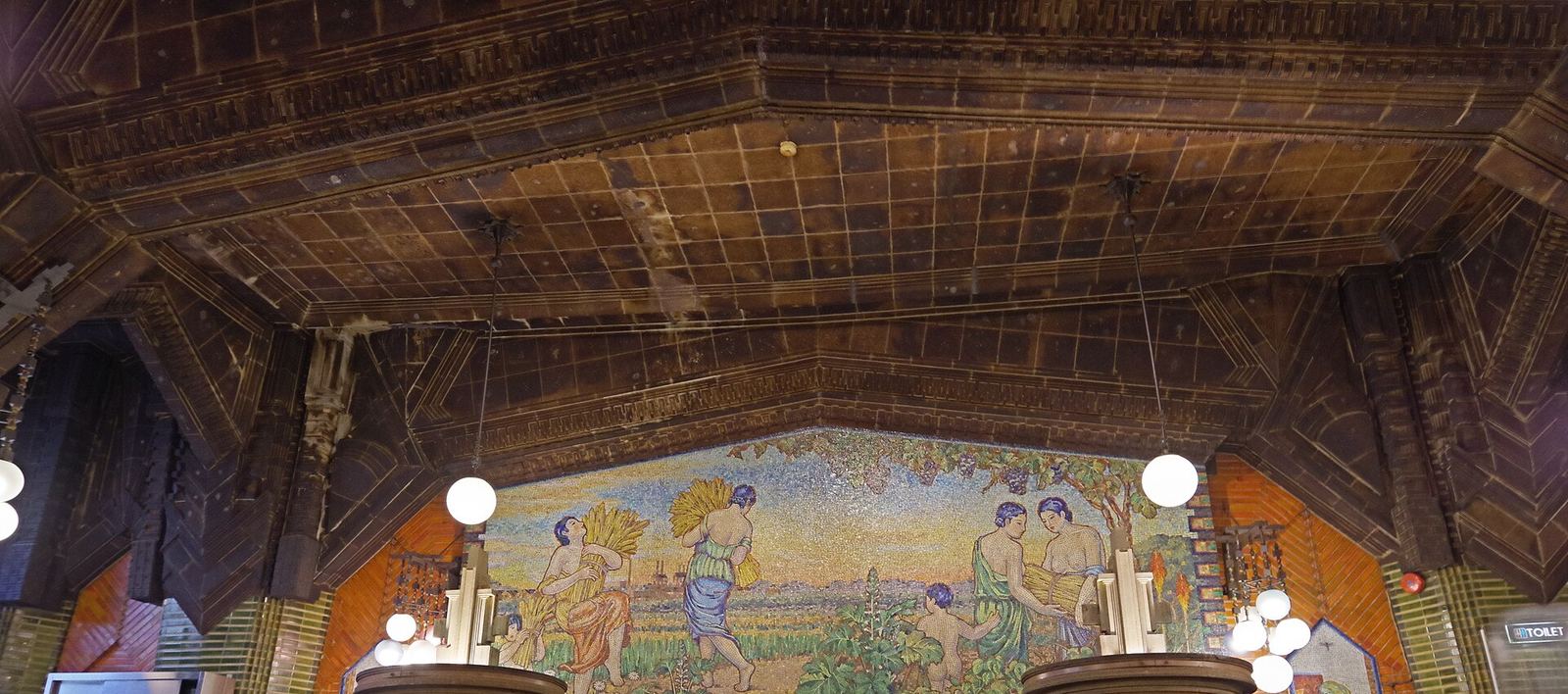 The 1934 hall of Beer Hall Lion Ginza 7-chome, with its dark coffered ceiling, globe lamps and a large glass mosaic of harvest figures above the bar