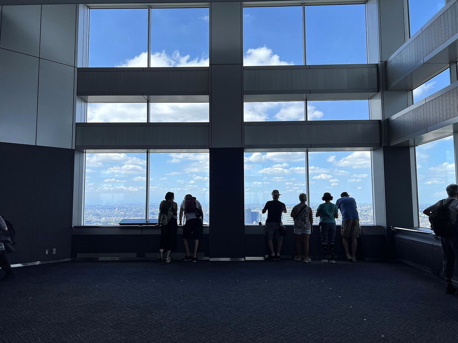 Visitors silhouetted against the tall windows of the Tokyo Metropolitan Government Building's observatory, looking out over the city