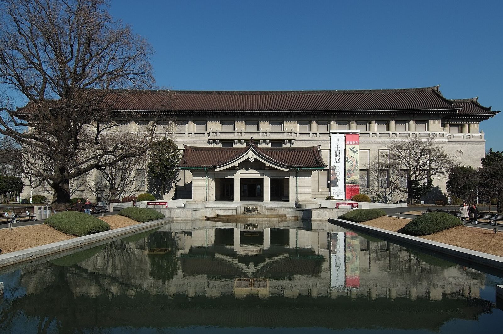 The Honkan of the Tokyo National Museum, a long building with a tiled Japanese roof, reflected in the pond in front of it in Ueno Park