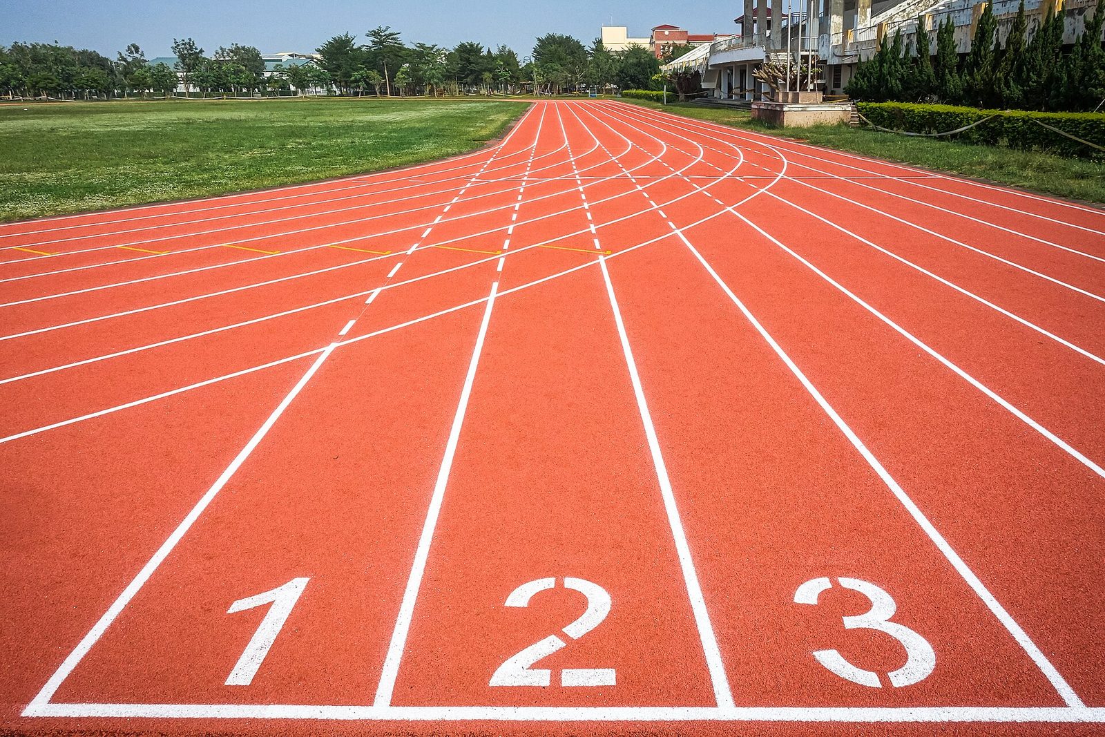 An empty red all-weather running track with lanes 1, 2 and 3 numbered in white at the start line, curving away towards the bend